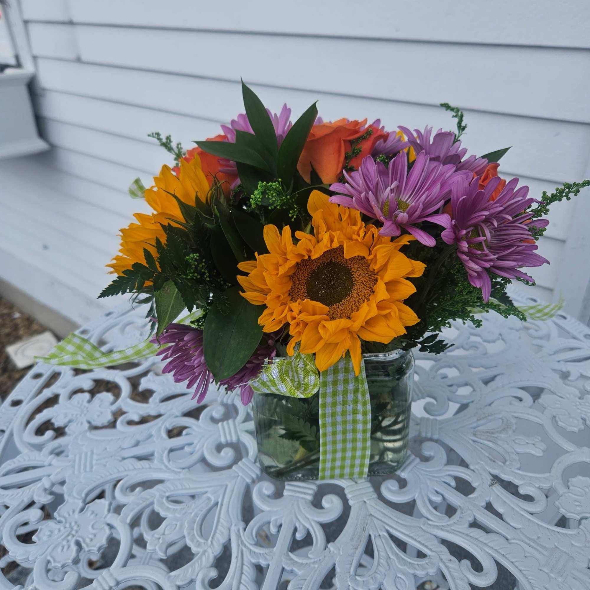 Sunflowers, lavender daisys, orange roses and solidago arranged in a glass cube