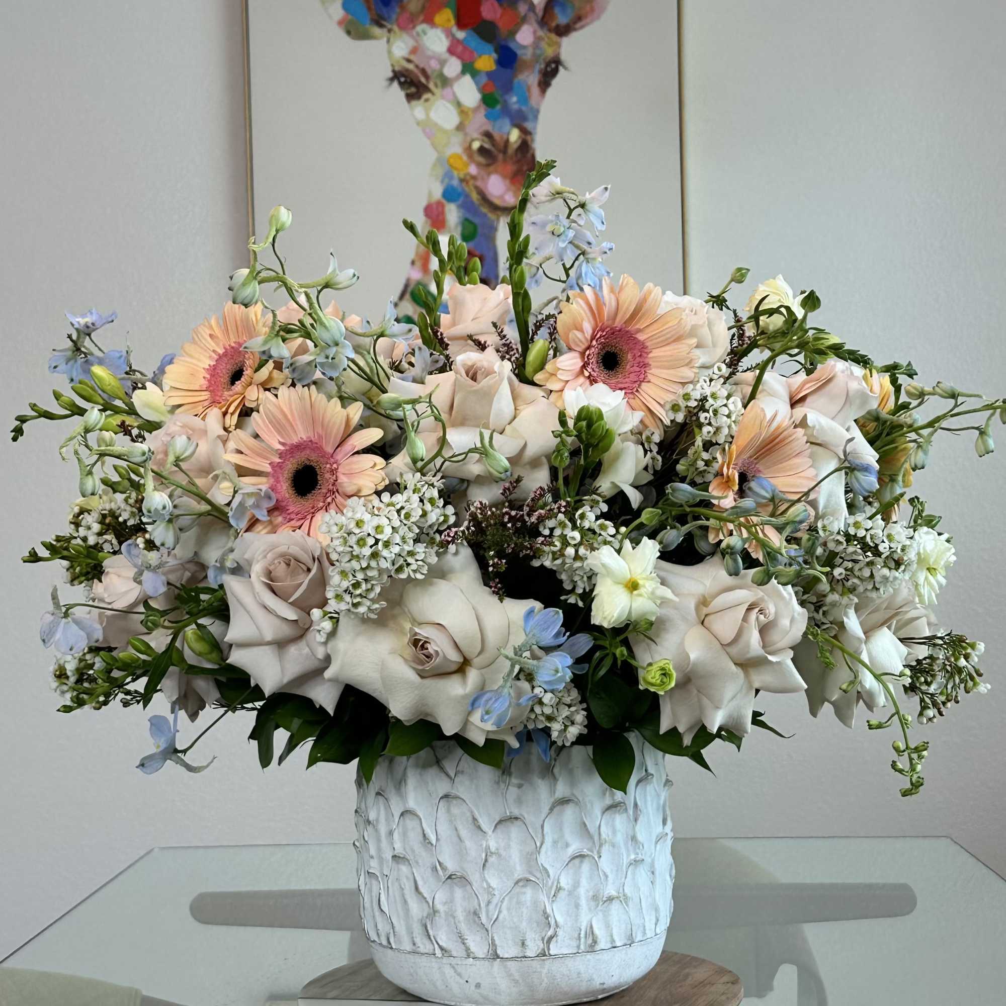 Garden-style arrangement featuring blush roses, peach gerbera daisies, delicate delphiniums, and lush
