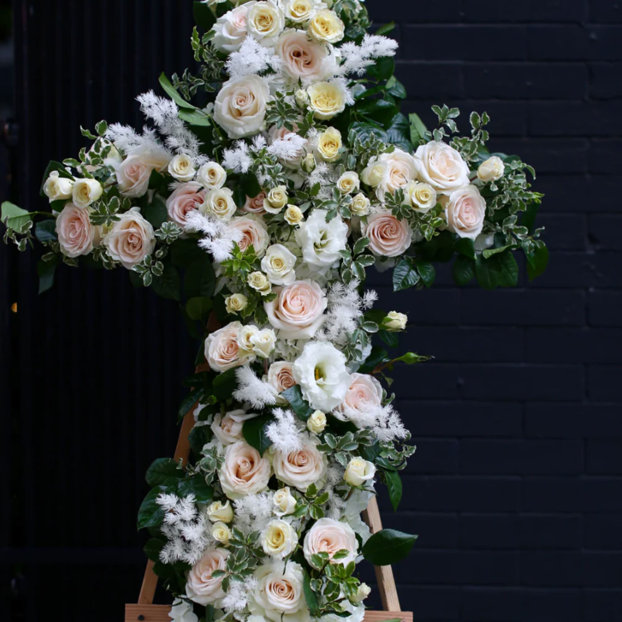 A solemn tribute featuring roses and lisianthus arranged in the shape of