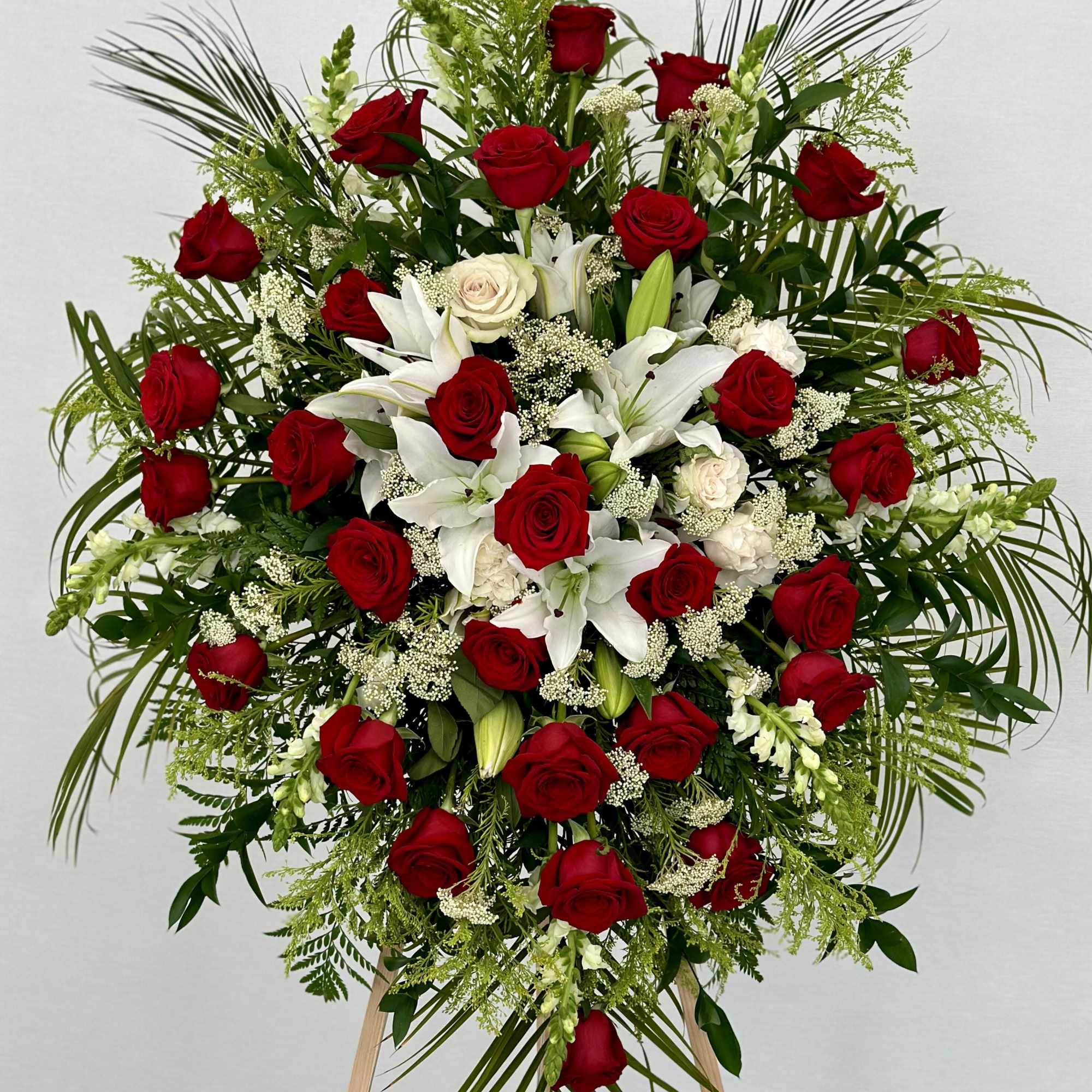 This funeral spray features deep red roses, symbolizing love and respect, alongside