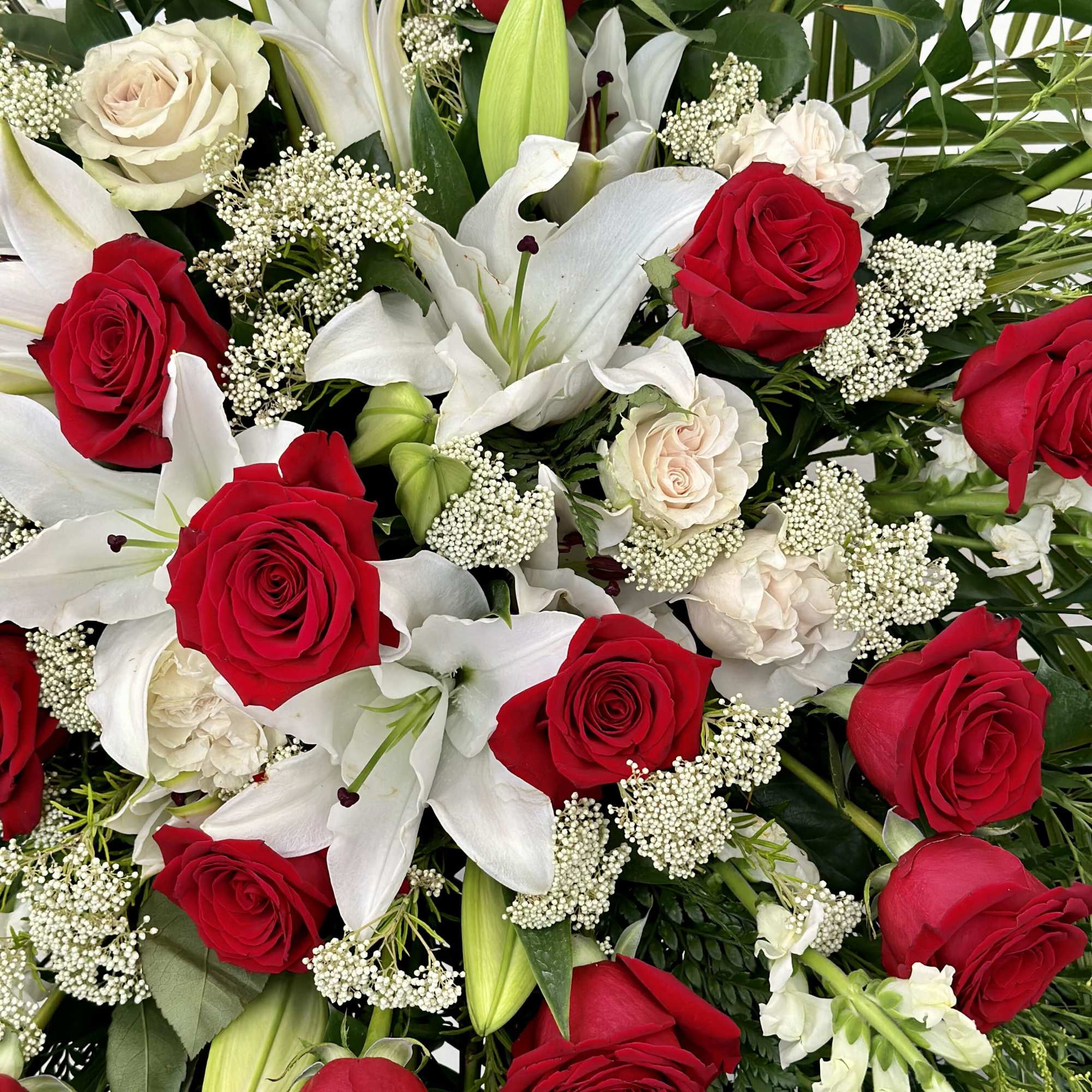 This funeral spray features deep red roses, symbolizing love and respect, alongside