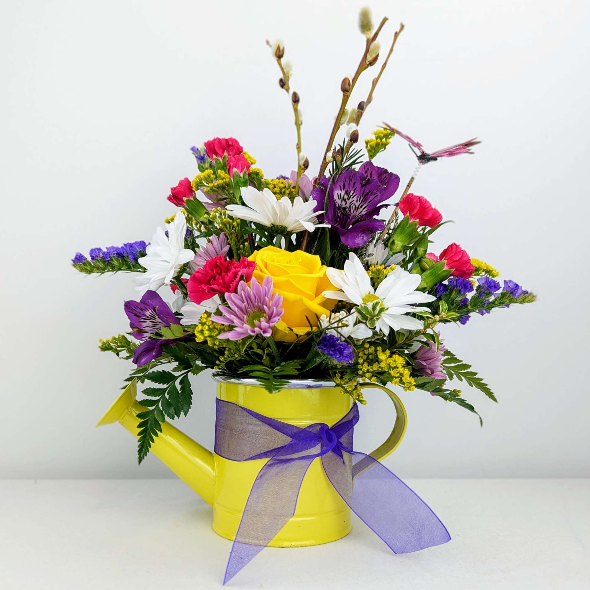 A springy collection of flowers in a bright watering can container (Assorted