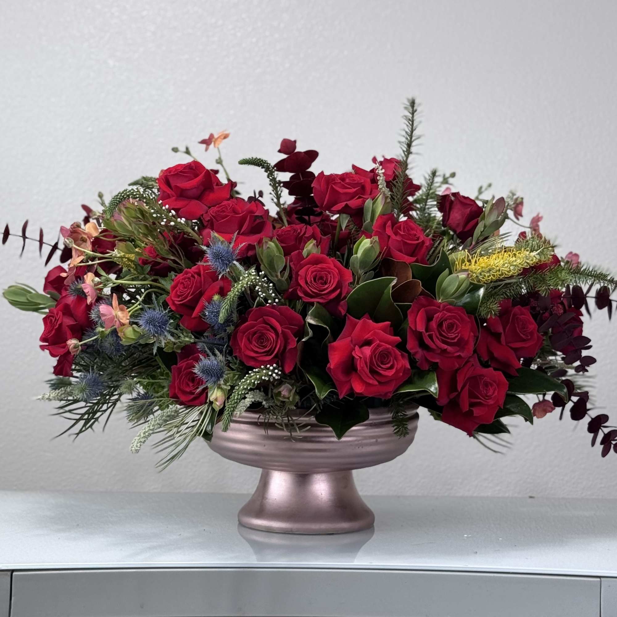 Featuring vibrant red roses complemented by a mix of fresh greenery, delicate