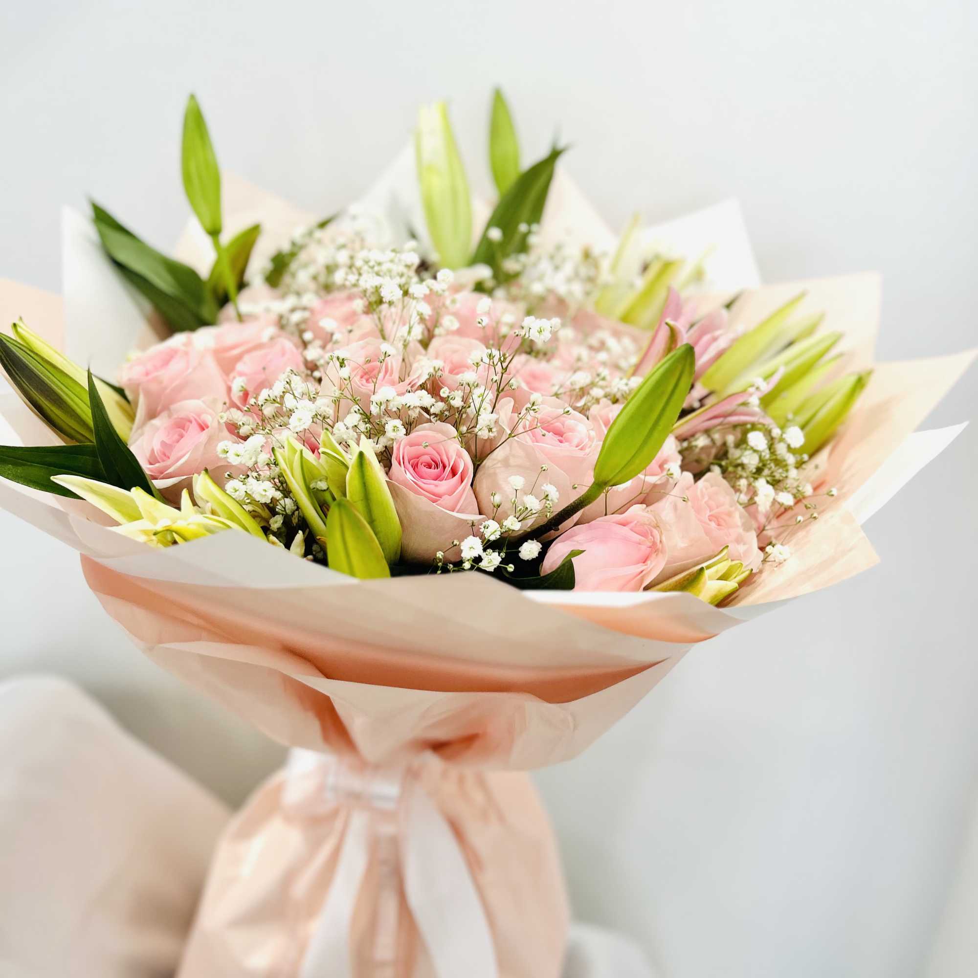 Medium hand wrapped bouquet with roses and lilies.