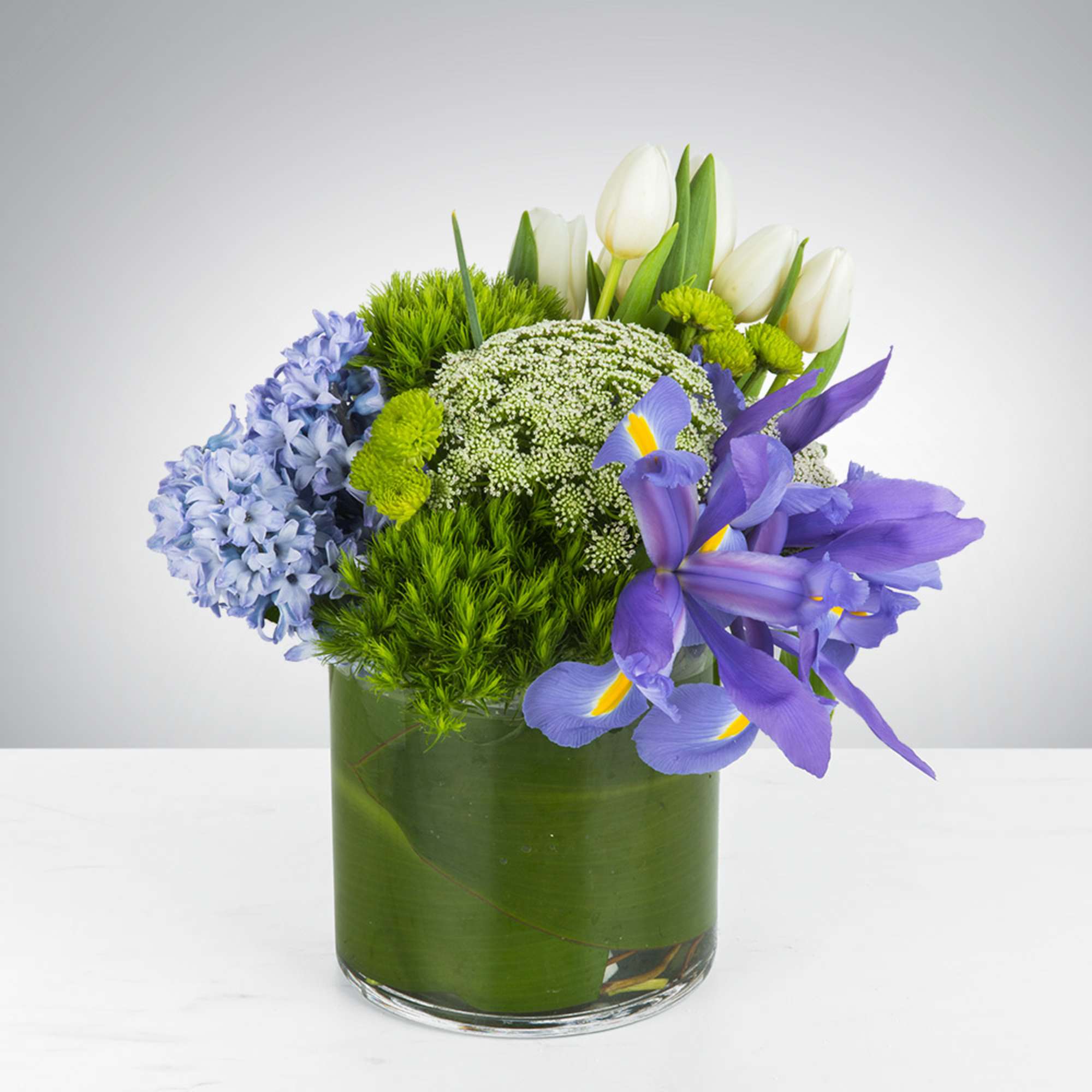 This arrangement includes green dianthus, blue iris, white tulips, hyacinths, and other
