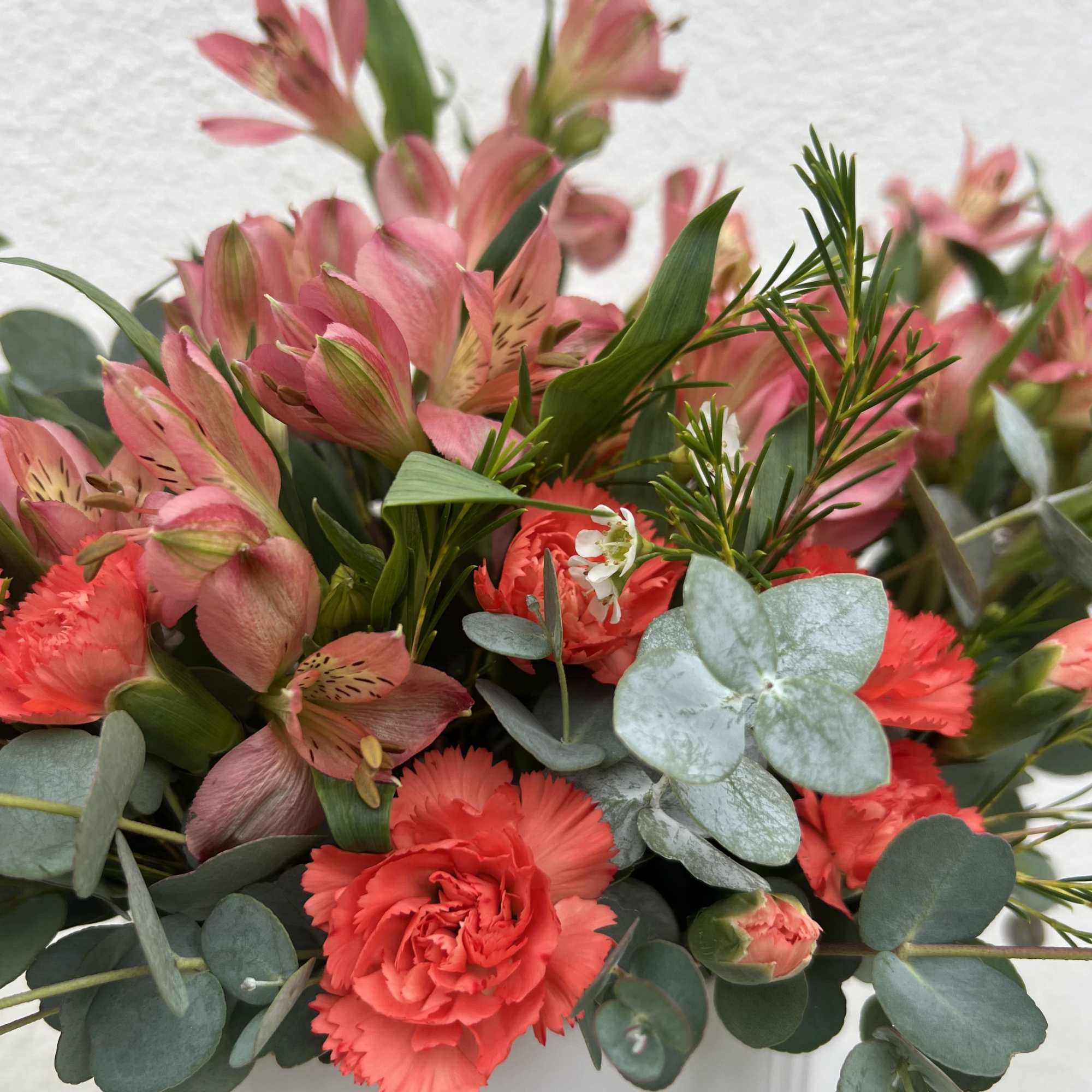 Pinkish Alstroemerias, Bright Orange Carnations, Waxflower and aromatic eucalyptus arranged in a
