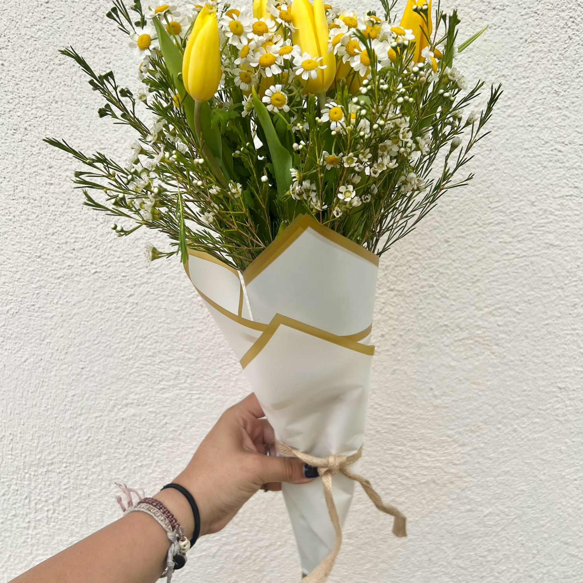 Sweet yellow Tulips, Daisies, and Waxflower are arranged in a handtied bouquet