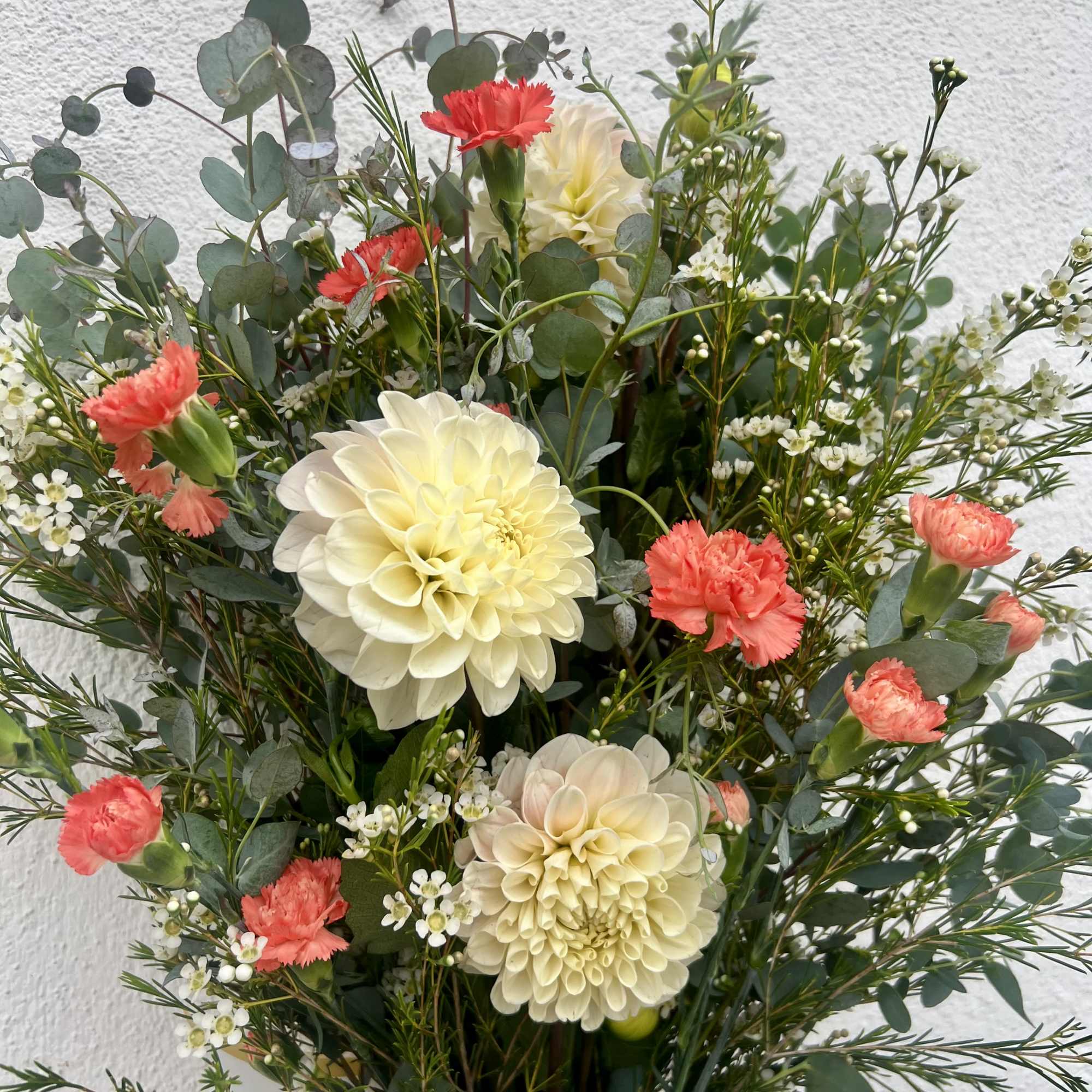 Incredible white/pink Dahlia&rsquo;s flourish alongside bright orange Carnations, Waxflower, and two different