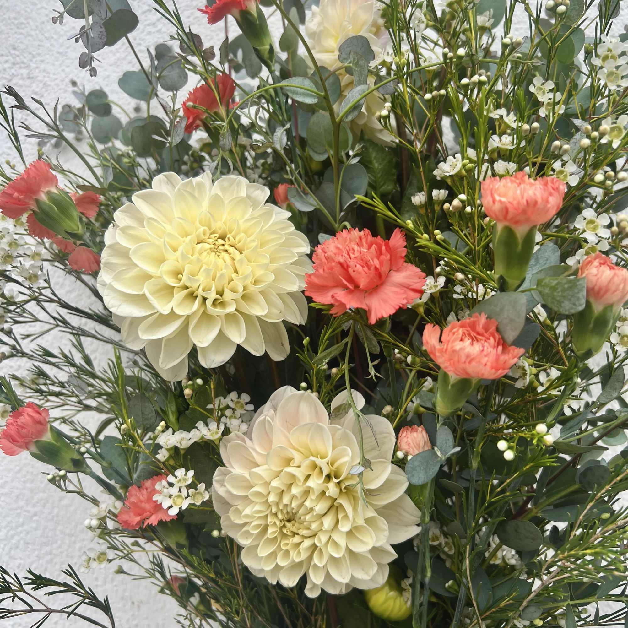 Incredible white/pink Dahlia&rsquo;s flourish alongside bright orange Carnations, Waxflower, and two different