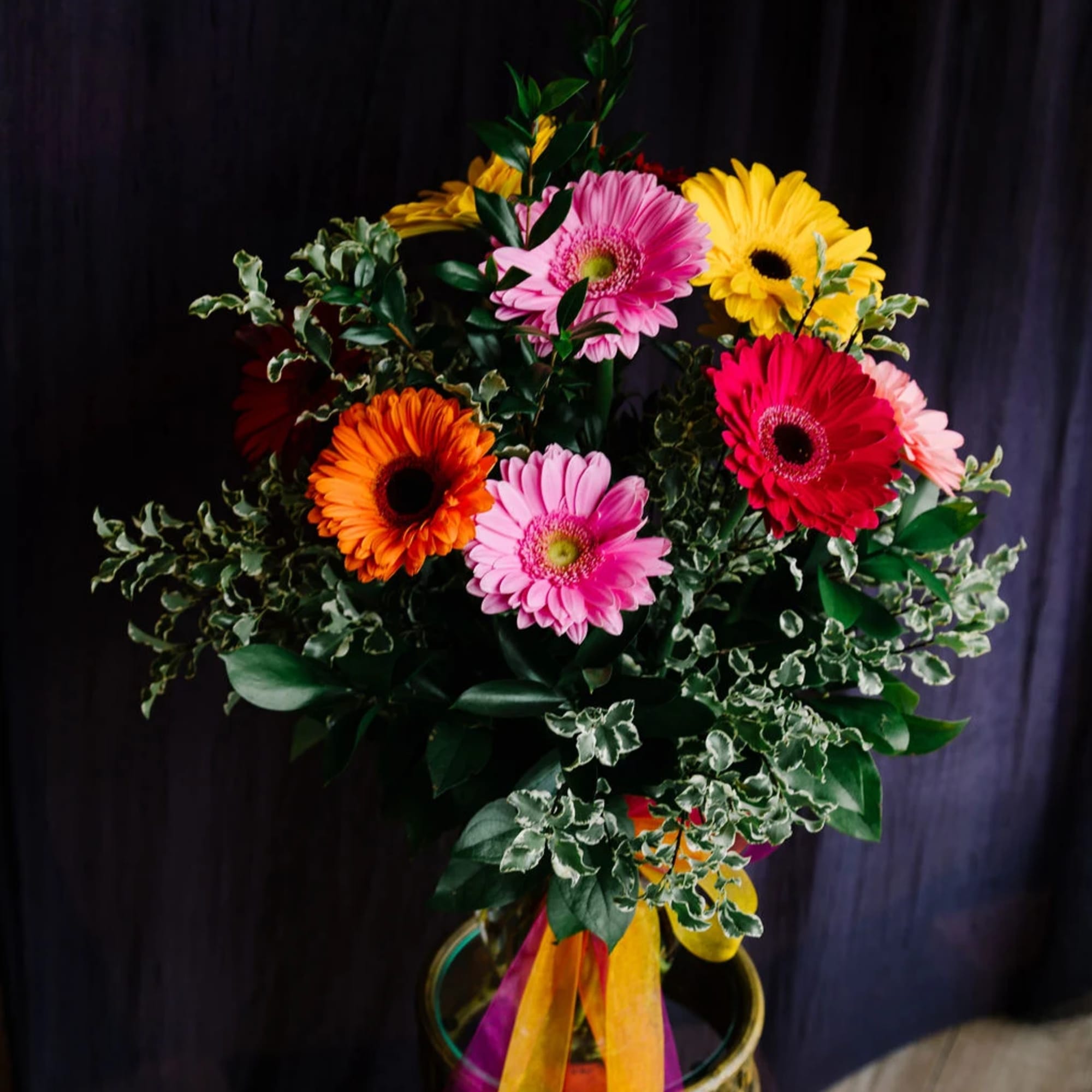 Nestled within a sleek glass vase, a kaleidoscope of 12 gerbera daisies