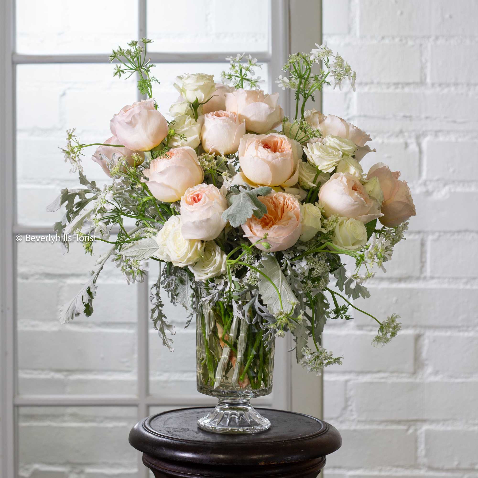 Nestled in a short glass vase, creamy romantic garden roses take center Nestled in a short glass vase, creamy romantic garden roses take center