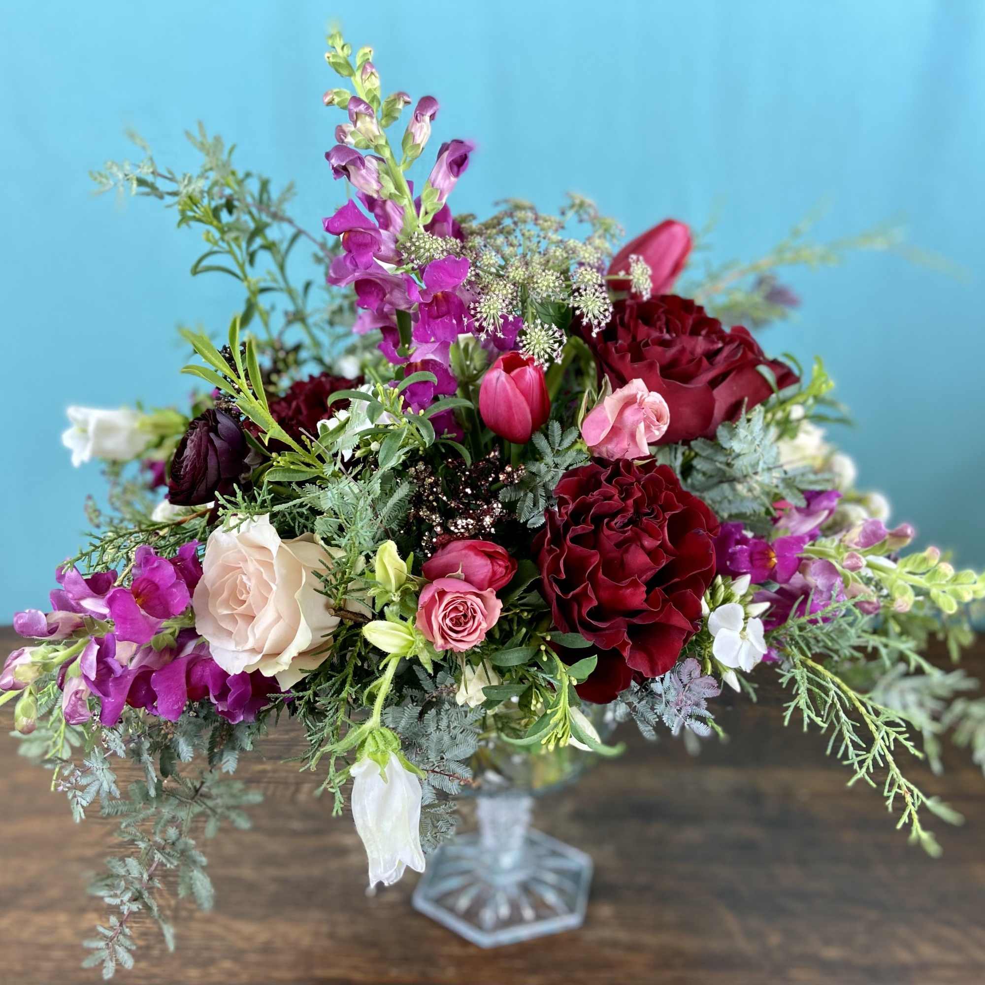 Low and lush floral arrangement in a short vase.  Typically includes