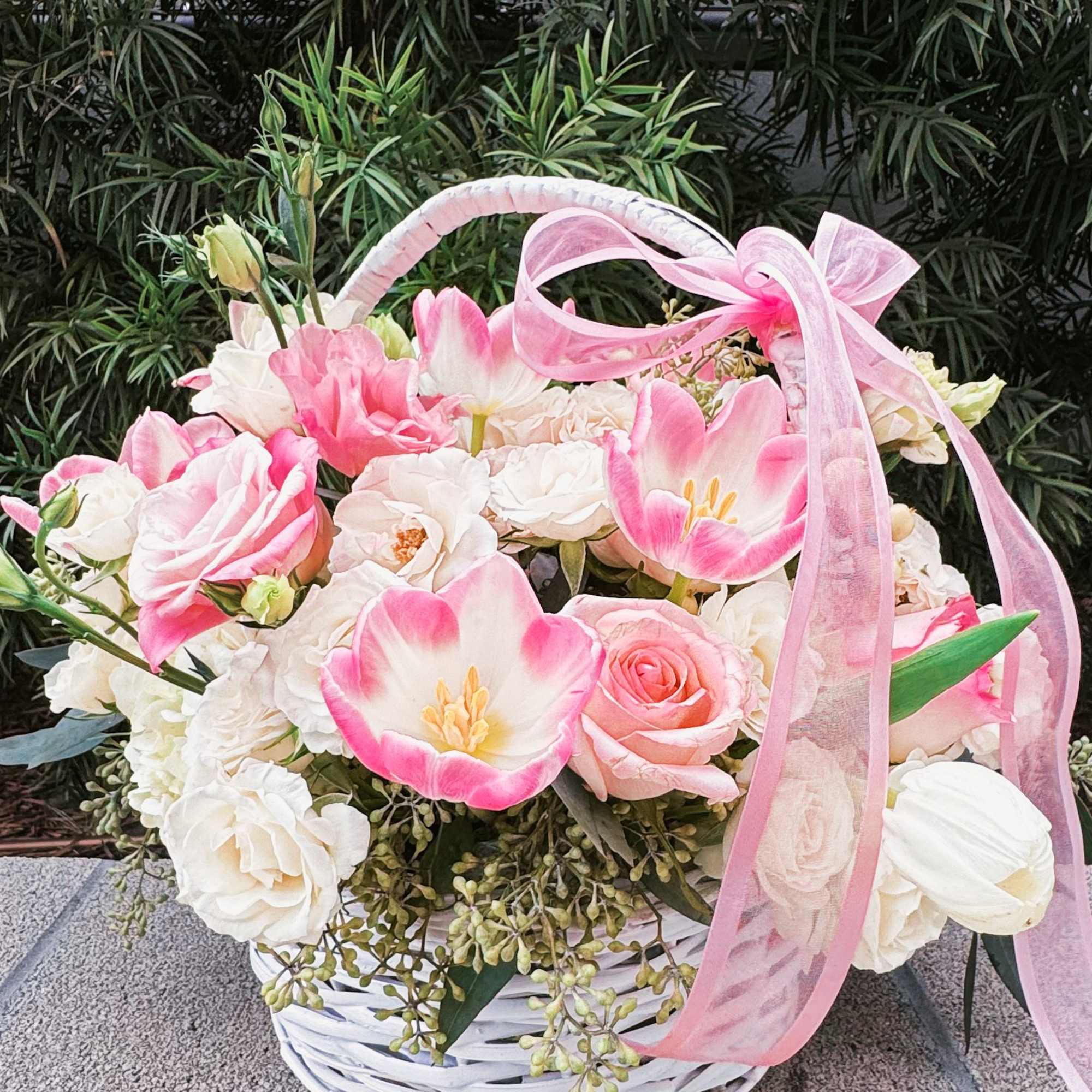 This charming basket bouquet brims with delicate pink roses, creamy white spray This charming basket bouquet brims with delicate pink roses, creamy white spray