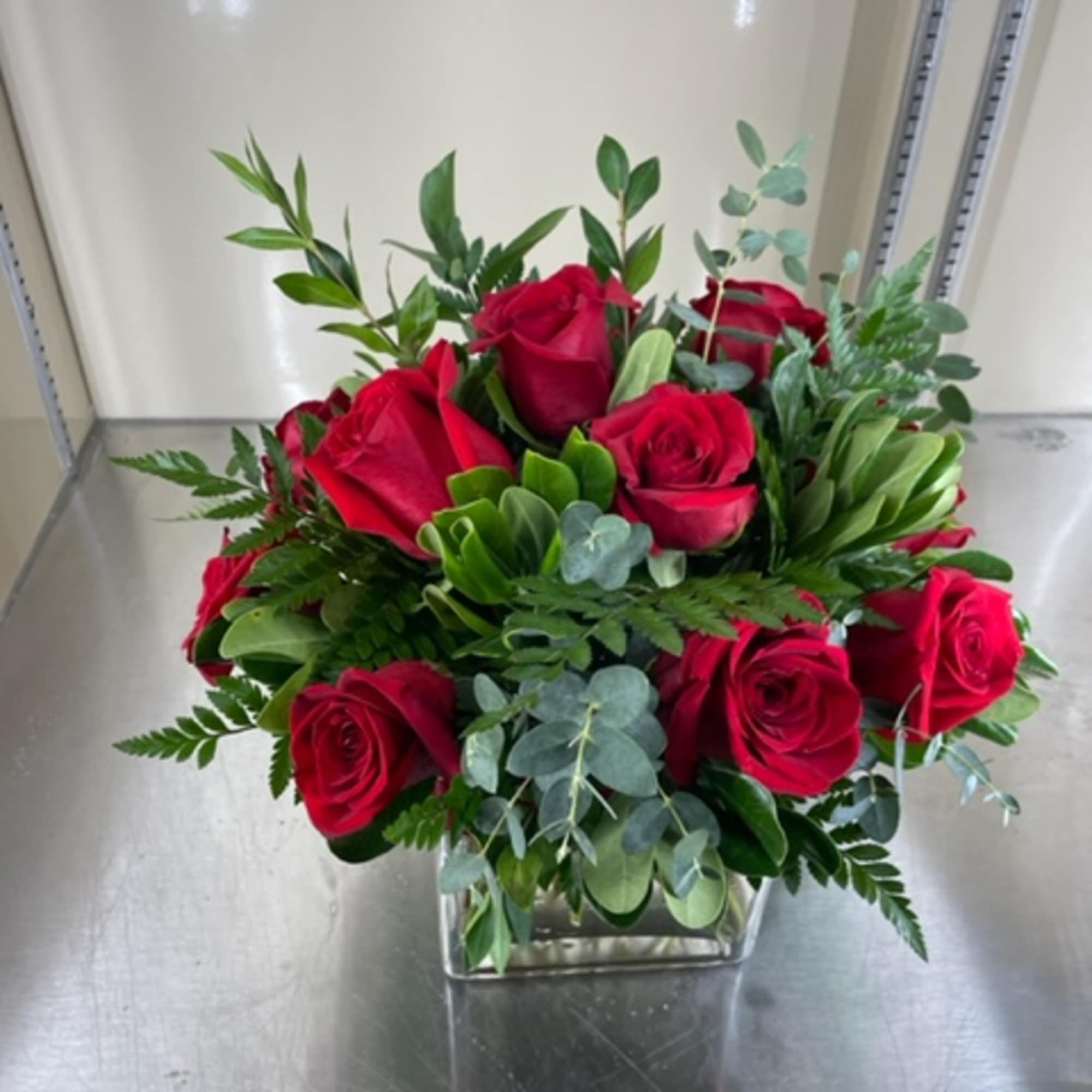 Red roses with mixed greens in a glass vase. Red roses with mixed greens in a glass vase.