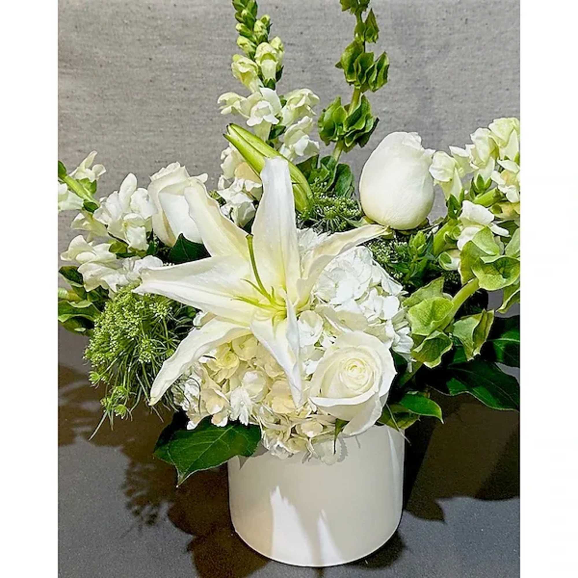 This calming arrangement of all white and green seasonal flowers, roses, lilies