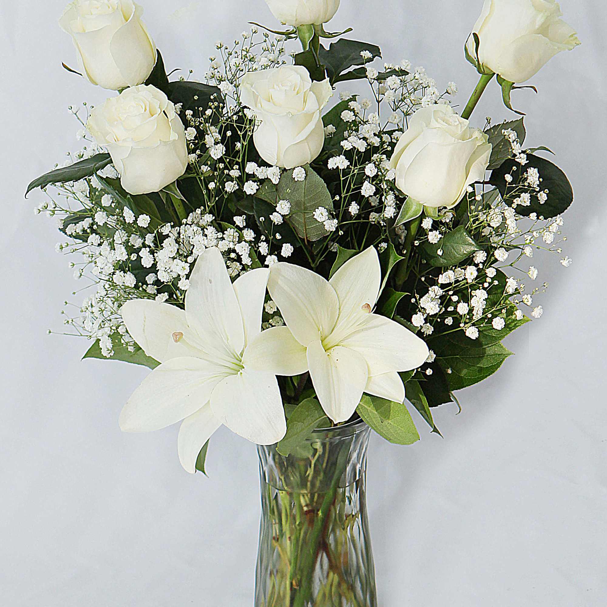 This all white arrangement includes. roses, lily and greenery.