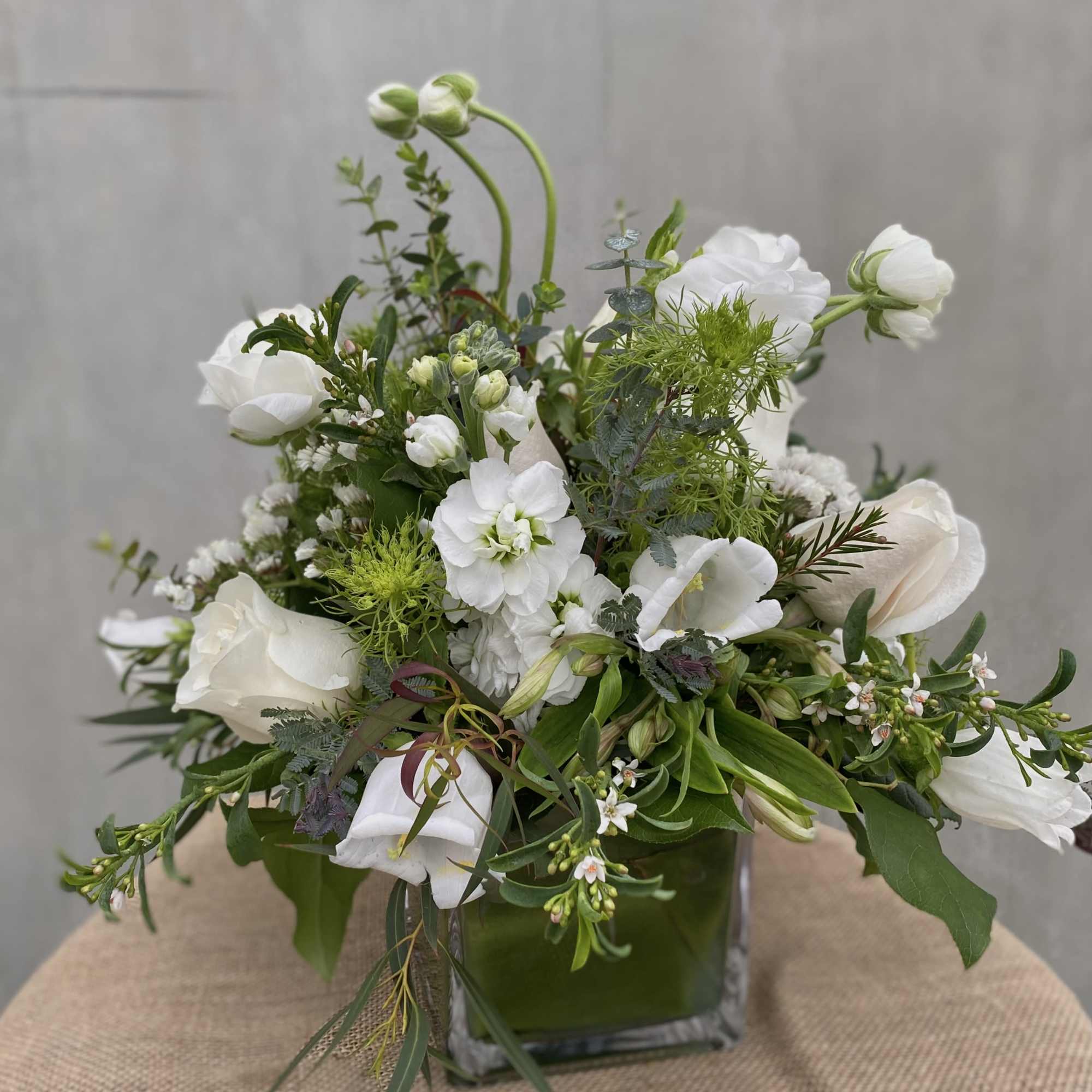 This elegant arrangement features white roses, ranunculus, and stock flowers, accented with