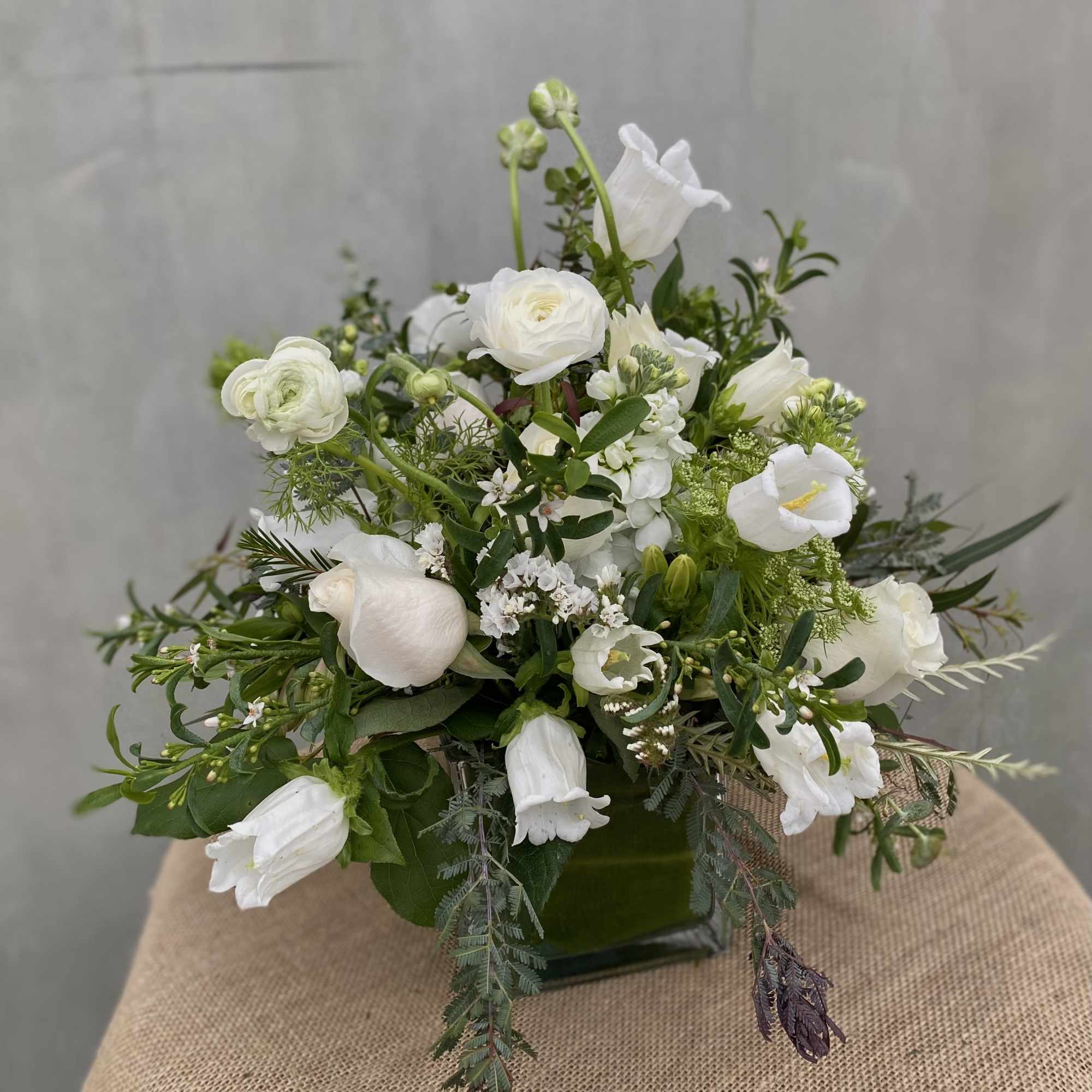 This elegant arrangement features white roses, ranunculus, and stock flowers, accented with