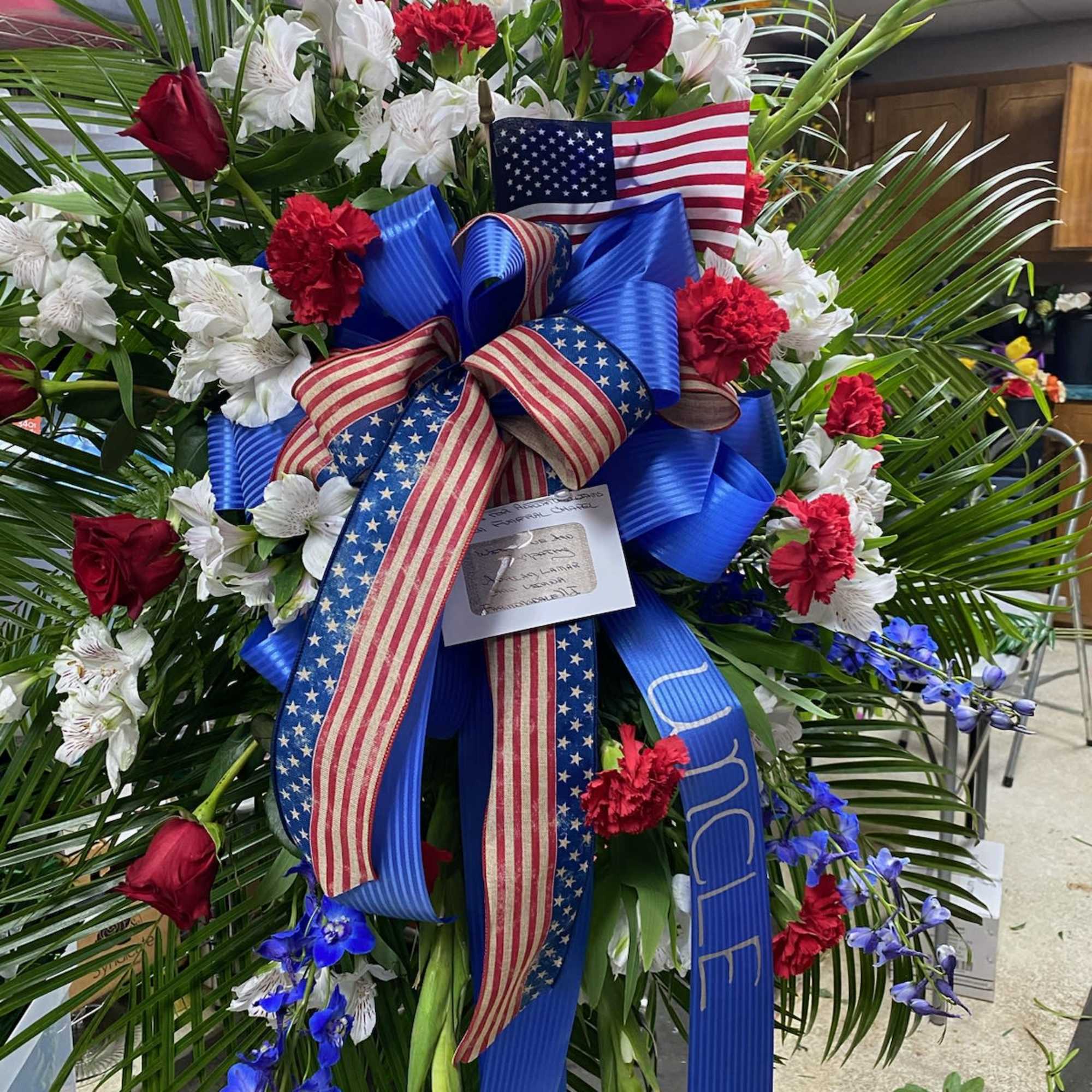 Featuring red, white and blue flowers along with a ribbon and flag Featuring red, white and blue flowers along with a ribbon and flag