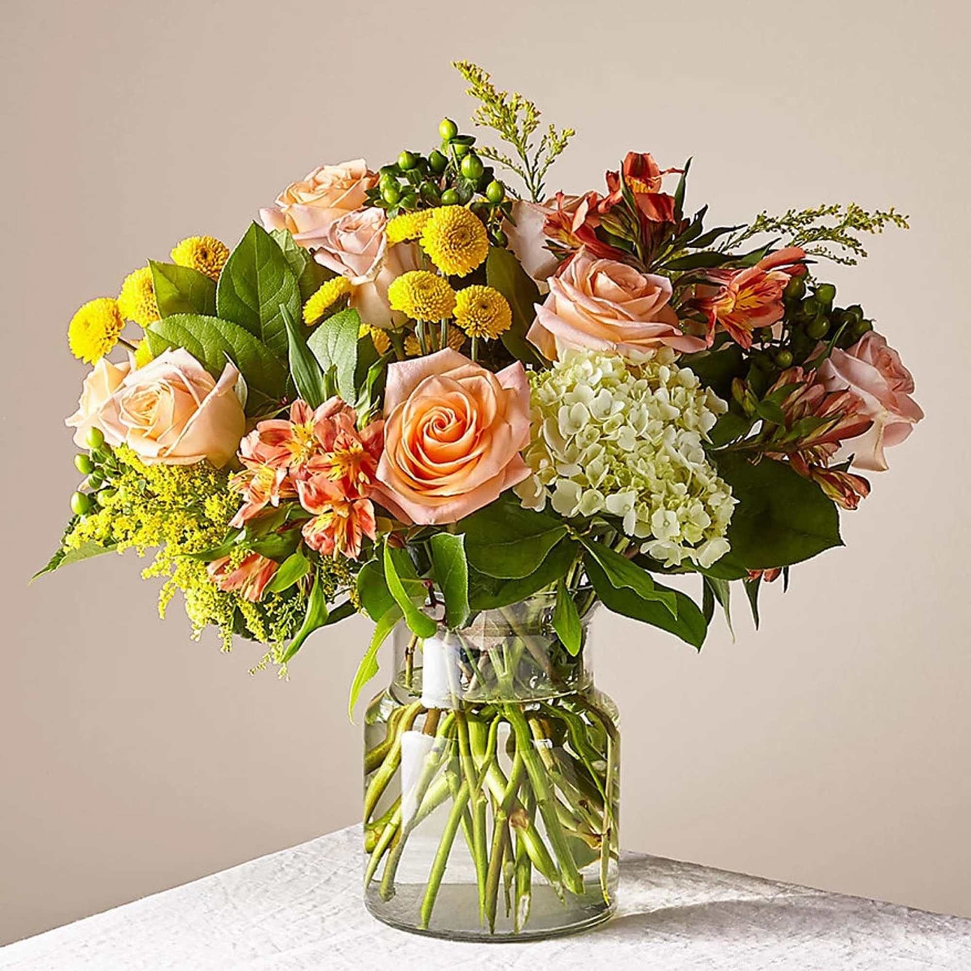 This warm and inviting arrangement features peach roses, alstroemeria, vibrant yellow Craspedia
