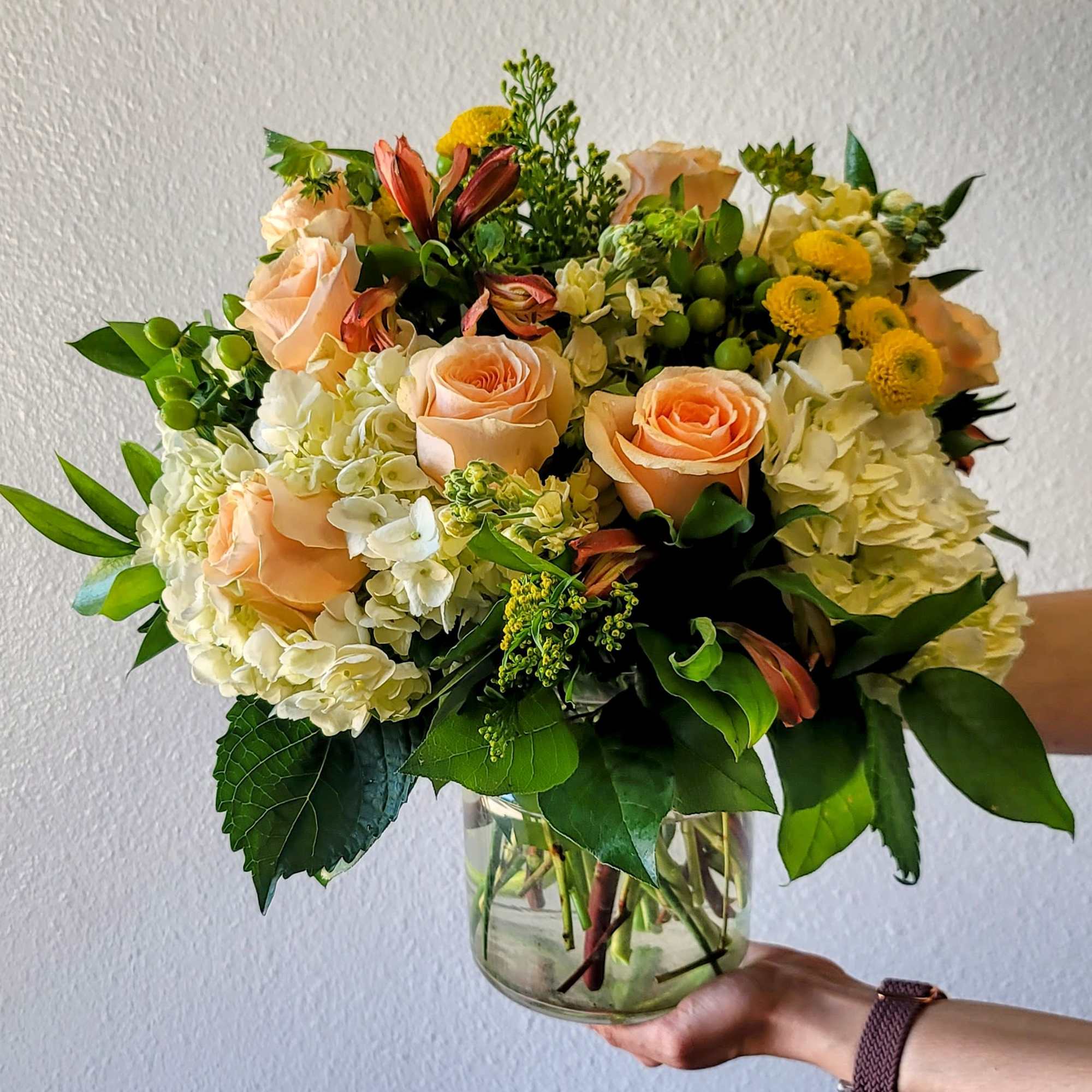 This warm and inviting arrangement features peach roses, alstroemeria, vibrant yellow Craspedia