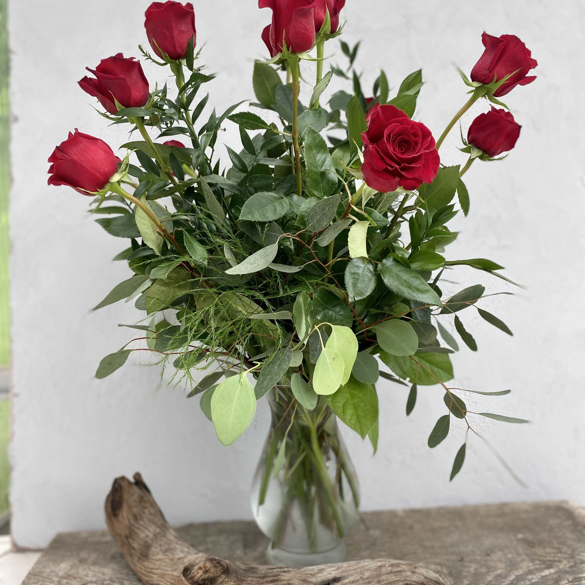 A dozen roses with mixed green filler in a tall glass vase.