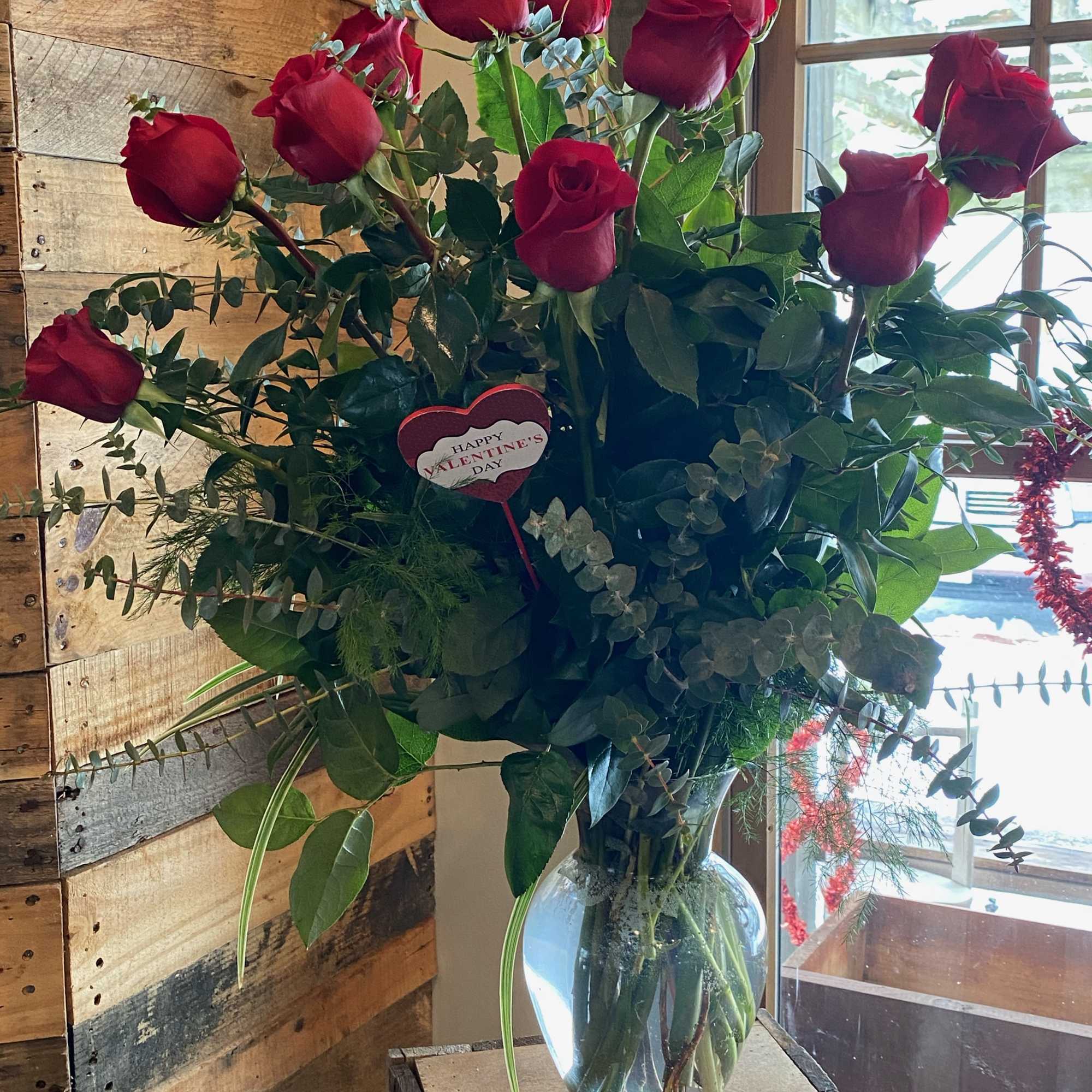A dozen roses with mixed green filler in a tall glass vase.