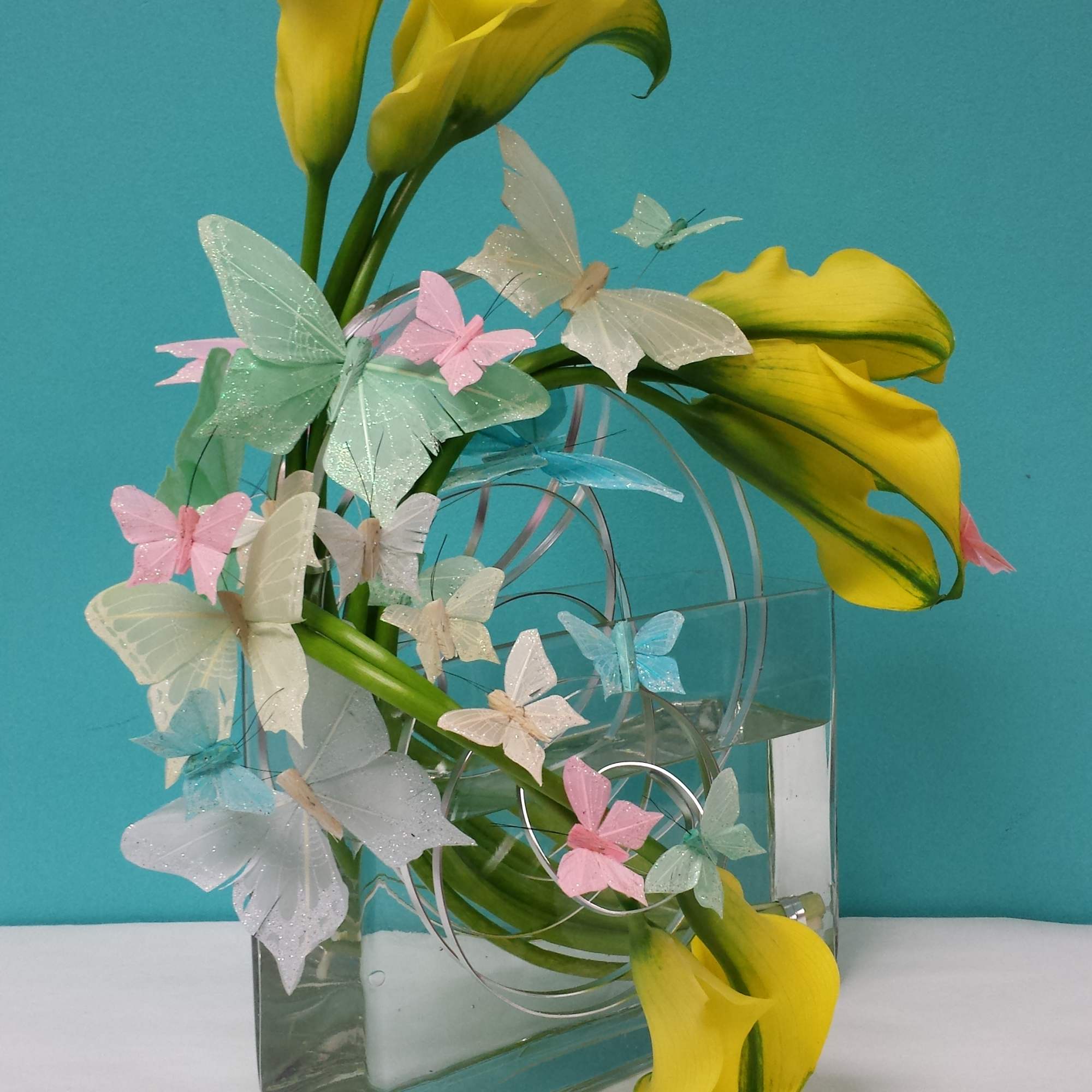 Callas in a square clear vase with butterflies.
There is a window off Callas in a square clear vase with butterflies.
There is a window off