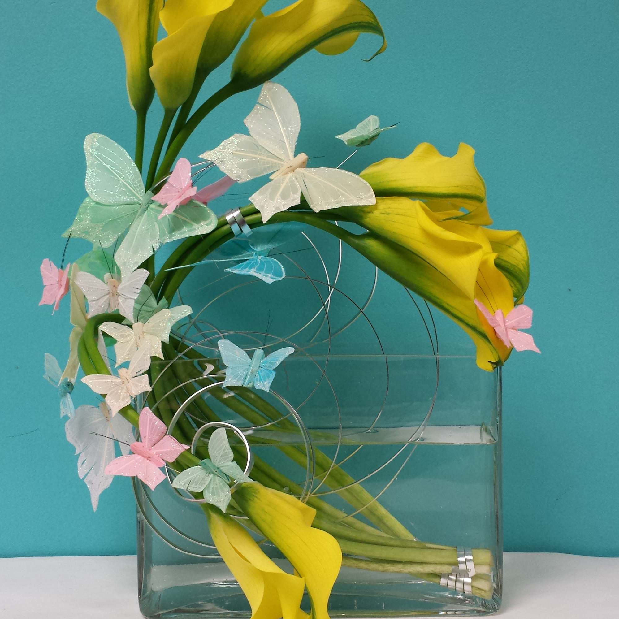 Callas in a square clear vase with butterflies.
There is a window off Callas in a square clear vase with butterflies.
There is a window off