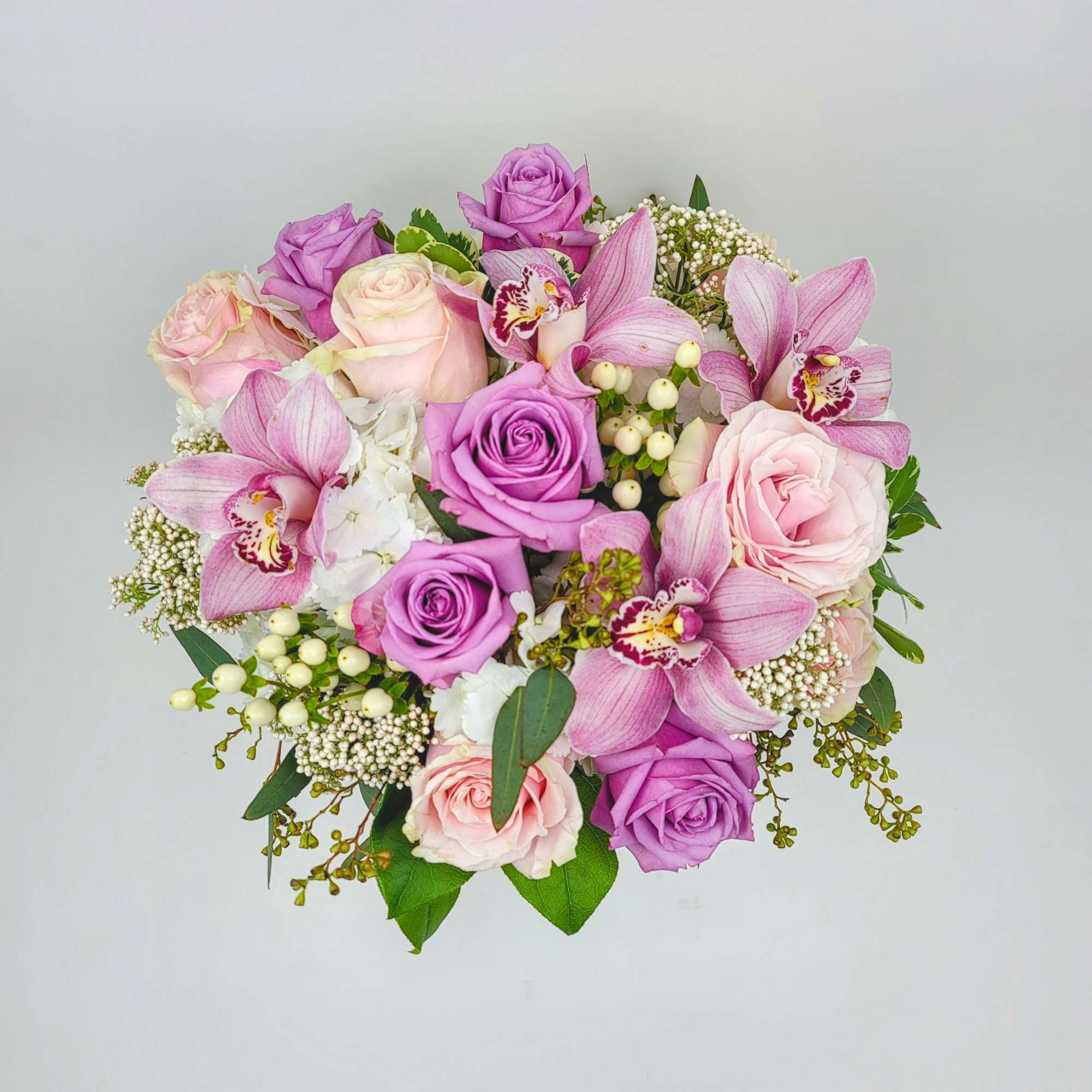 In a clear vase an arrangement with roses, hydrangeas,  cymbidium orchids