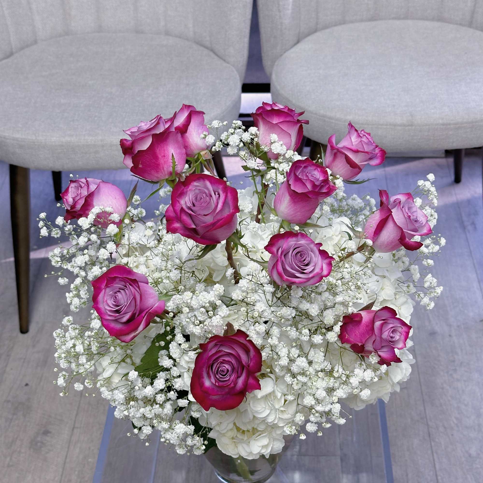 One dozen purple roses in a vase, accompanied with white hydrangeas and