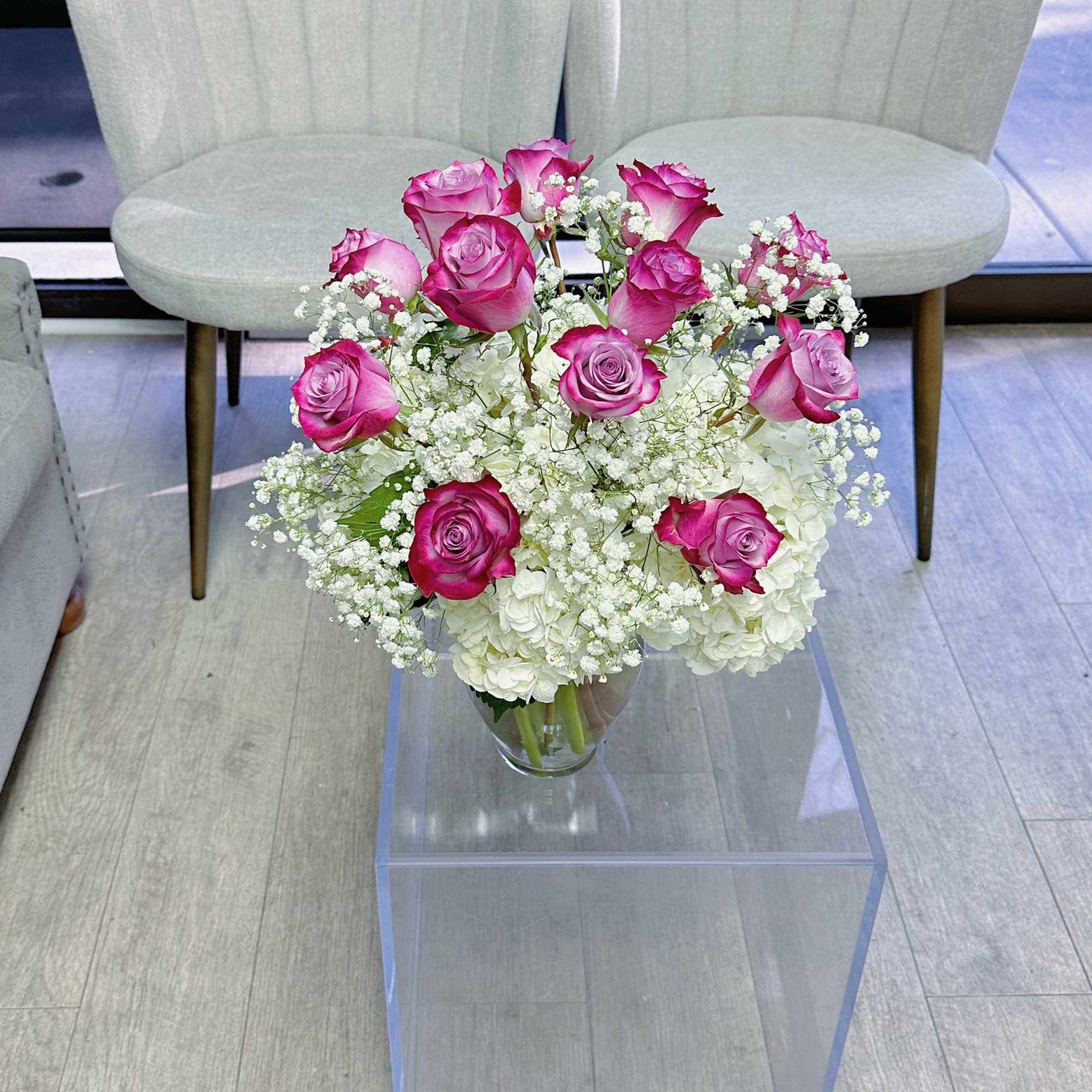 One dozen purple roses in a vase, accompanied with white hydrangeas and