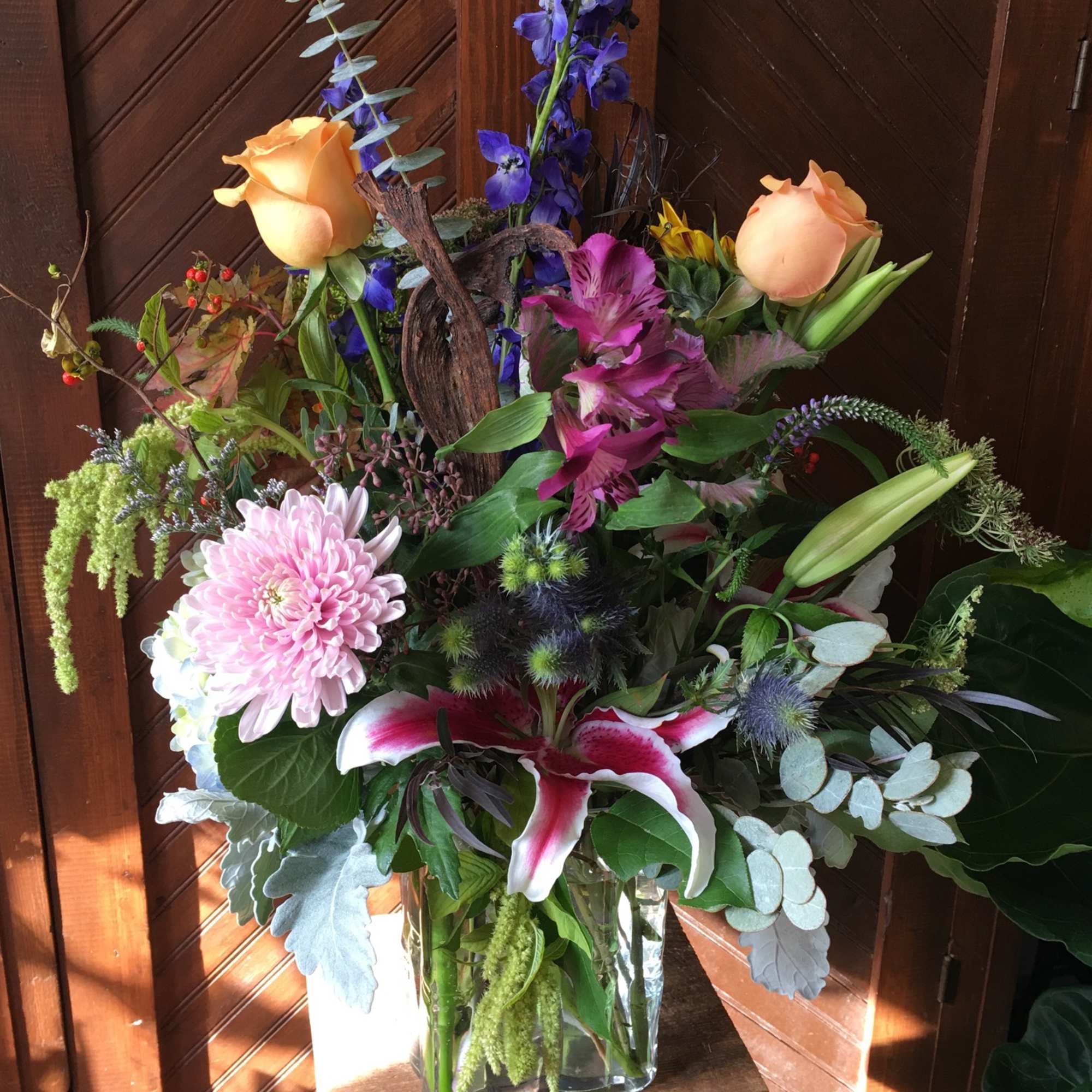 Assorted seasonal flowers and greenery in a cylinder or rectangle vase. 