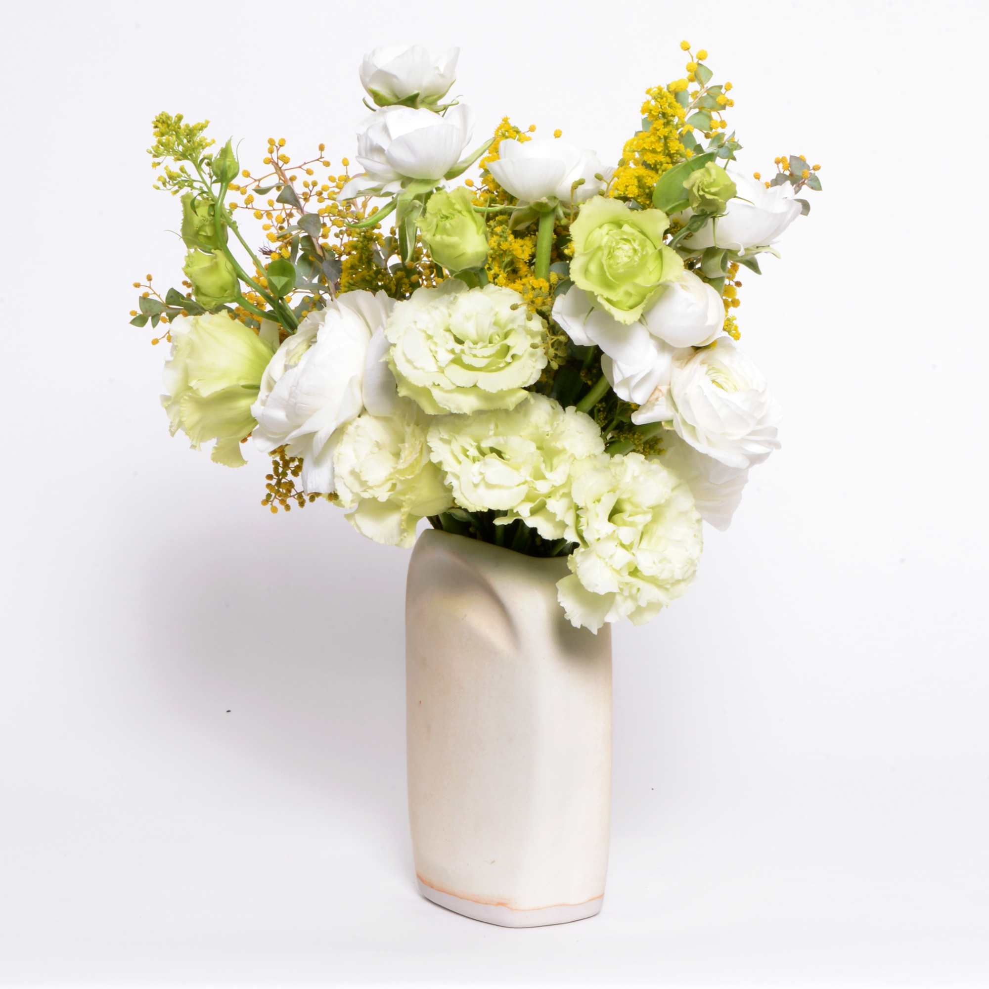 An arrangement of cream and white seasonal flowers in a handmade ceramic