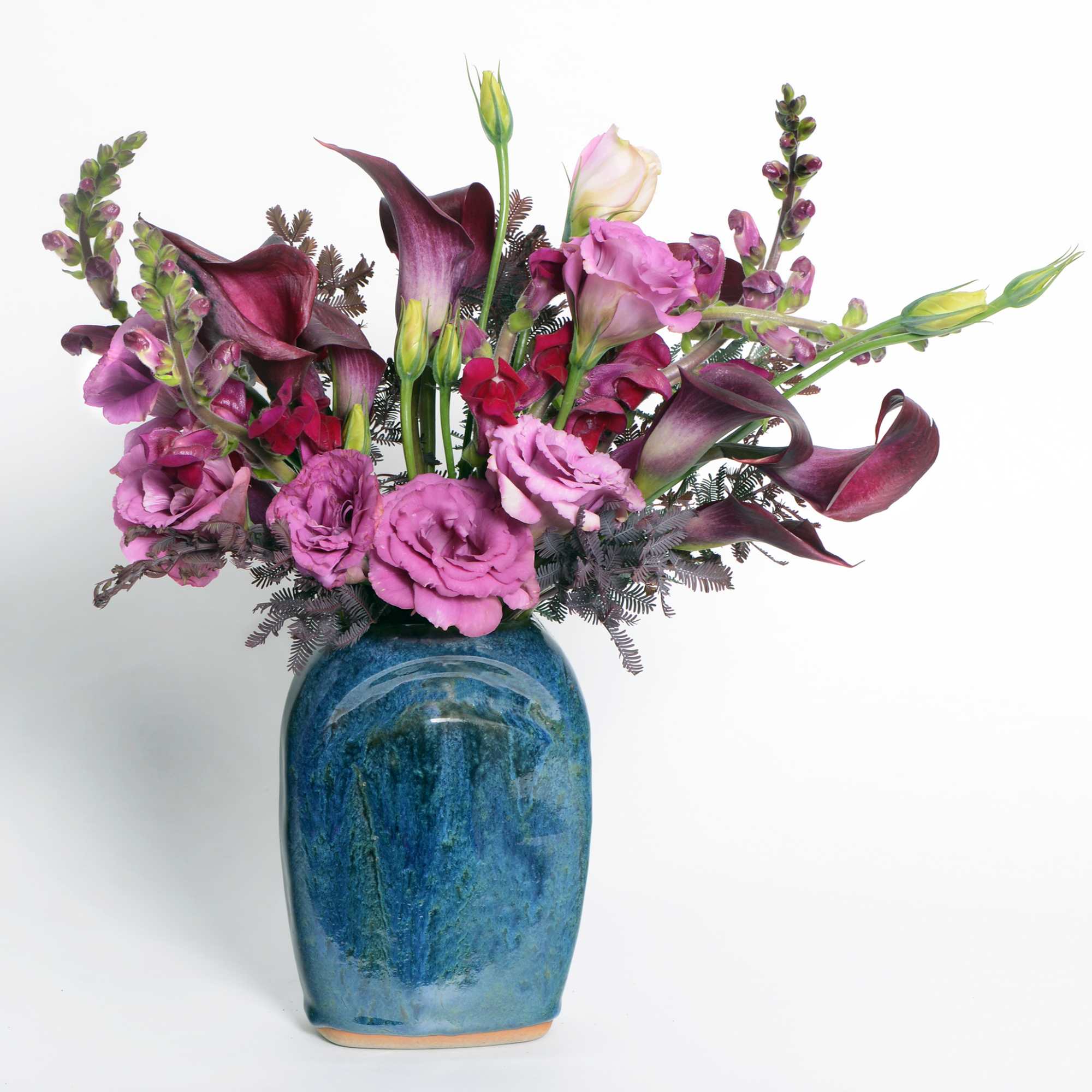 An arrangement of burgundy calla lilies, purple lisianthus and purple snapdragons in
