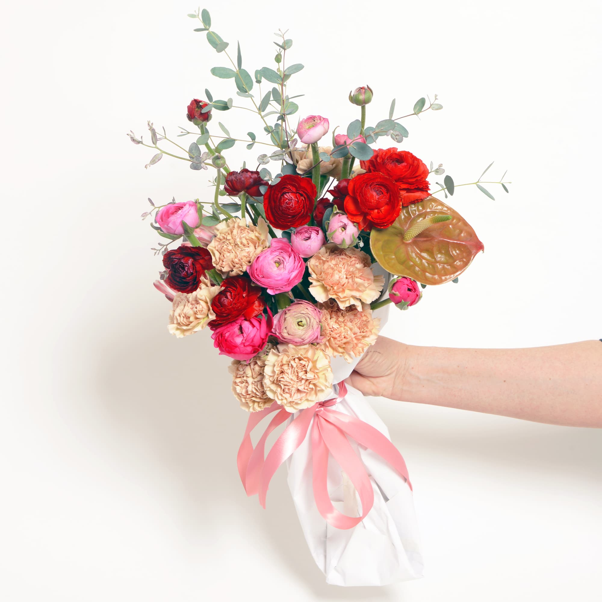 A hand tied wrapped bouquet of red and pink seasonal flowers, designers