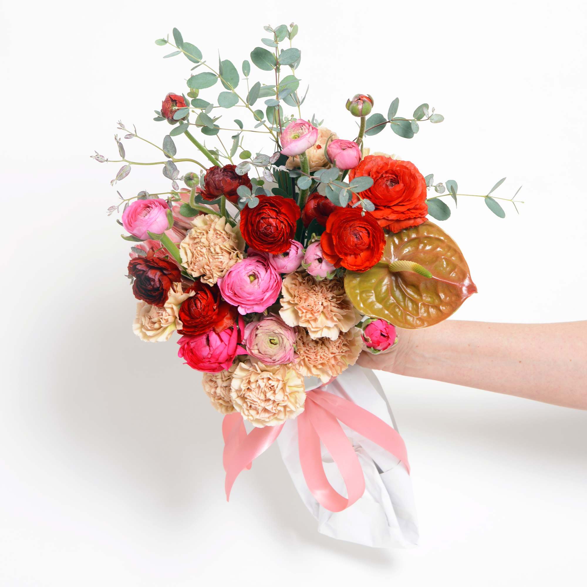 A hand tied wrapped bouquet of red and pink seasonal flowers, designers