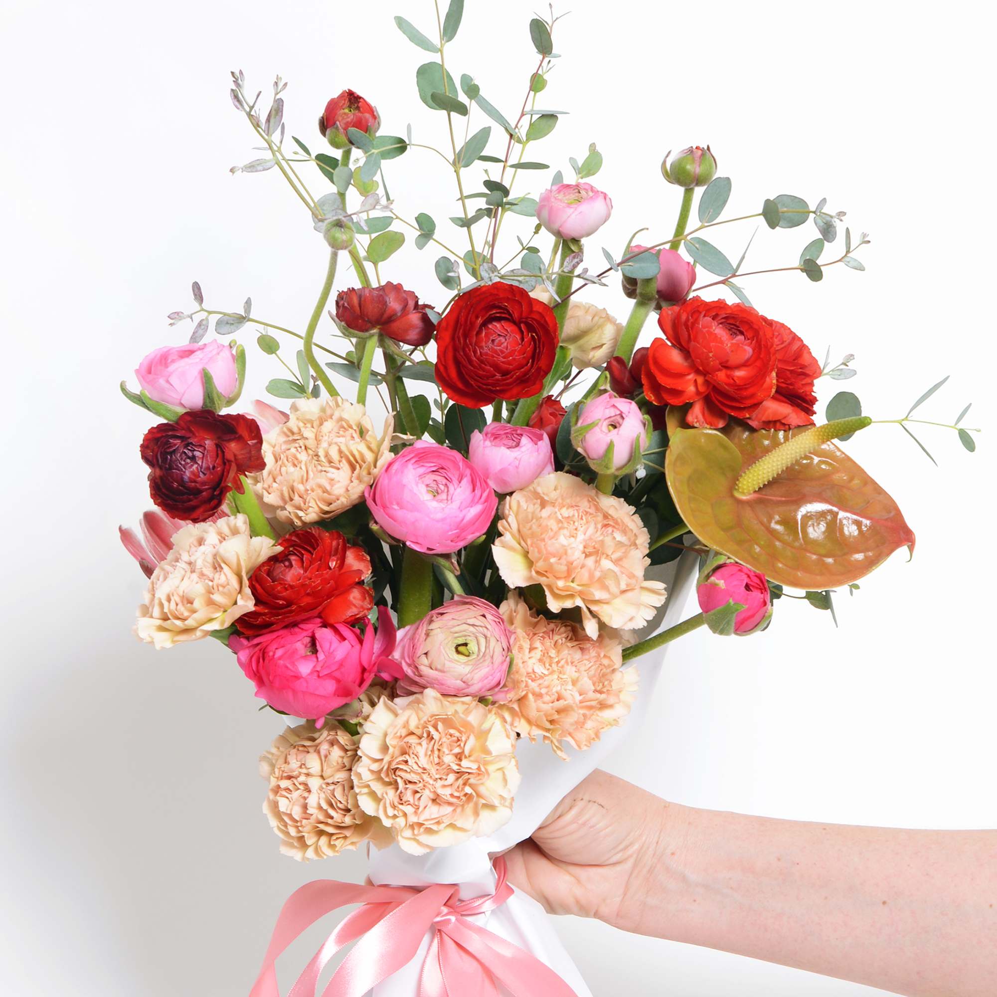 A hand tied wrapped bouquet of red and pink seasonal flowers, designers