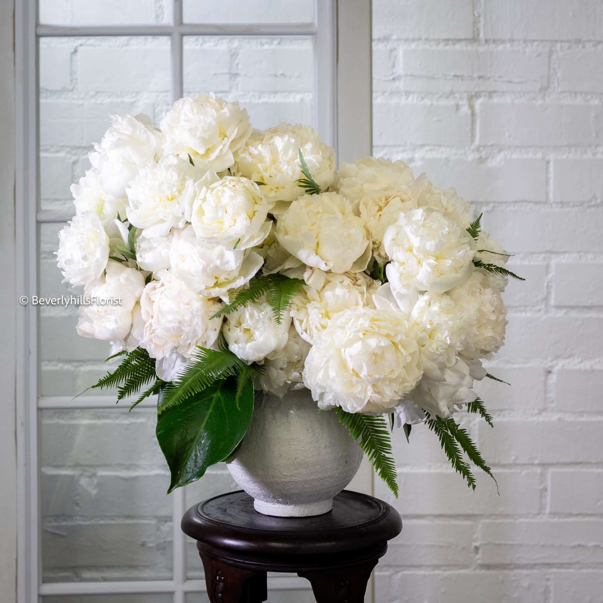  A lavish arrangement of over 20 pristine white peonies nestled within