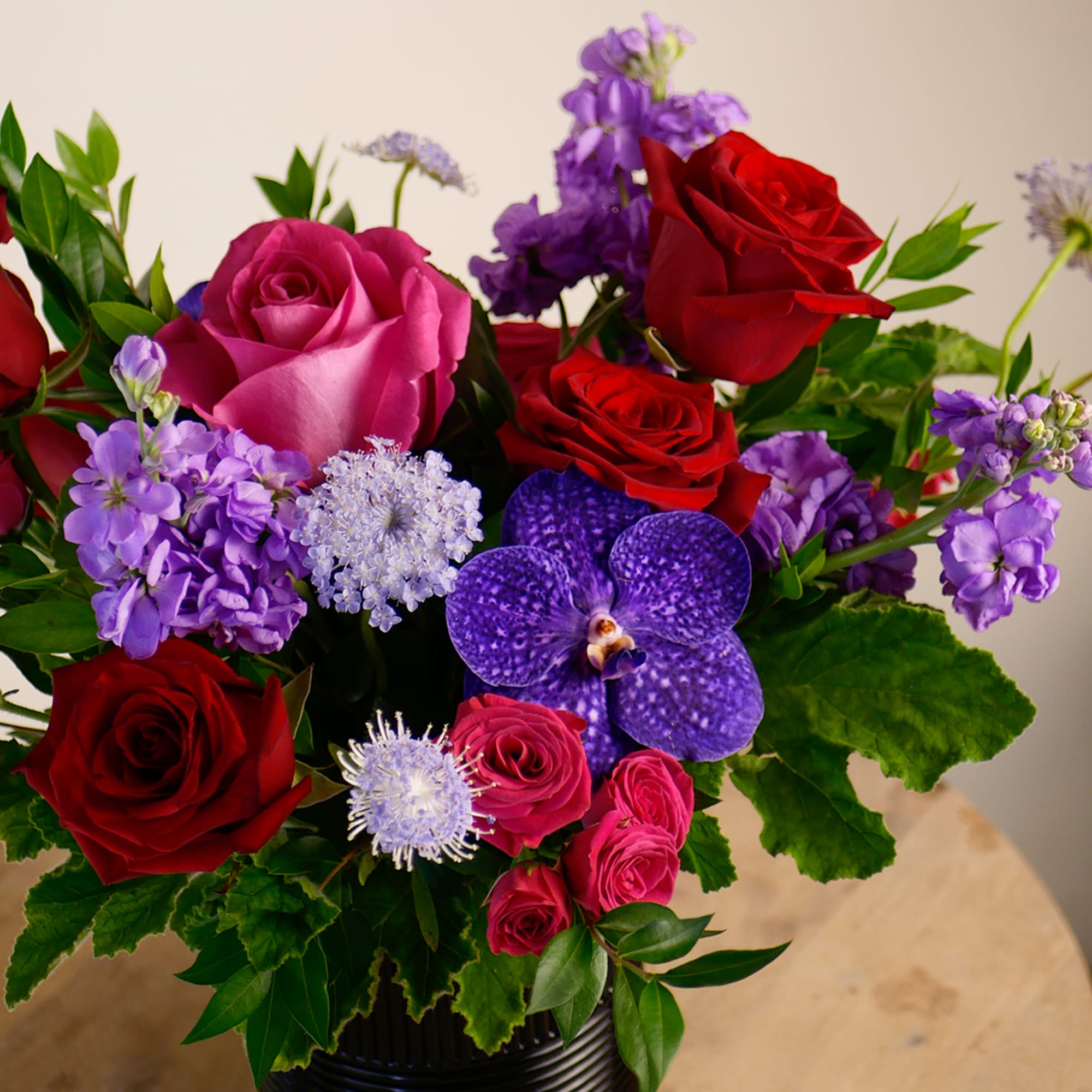 This romantic arrangement features rich jewel tones of deep reds, fuchsia, and