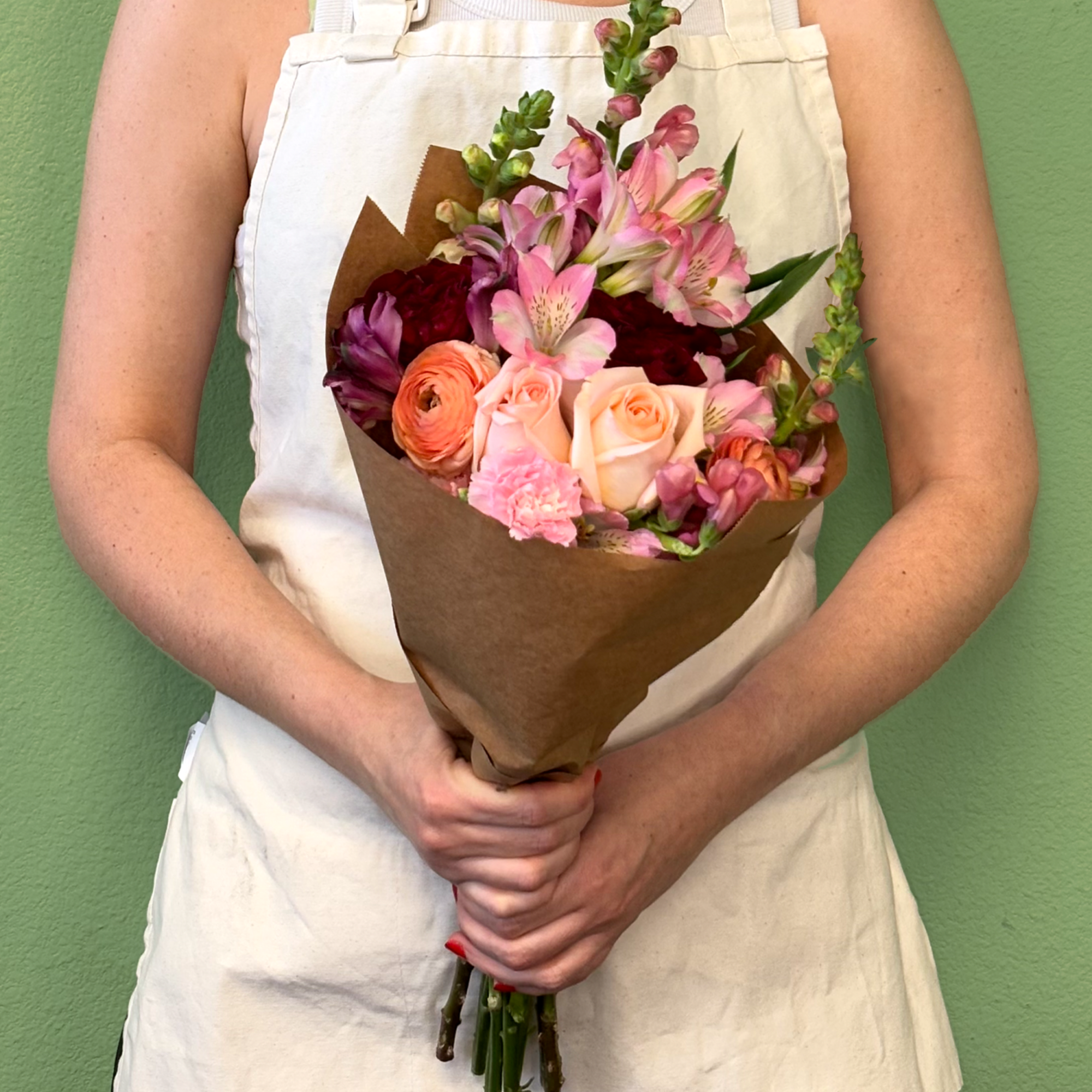 A charming wrapped bouquet that showcases a pink, peach, and red palette.