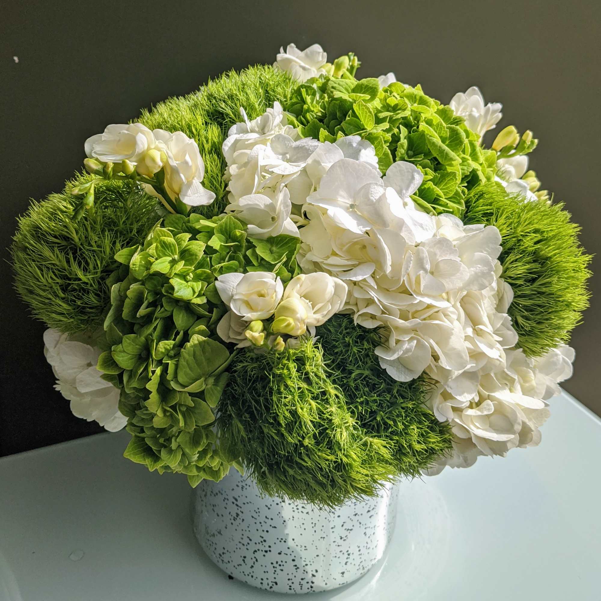 A designers choice arrangement of white and green flowers that will vary