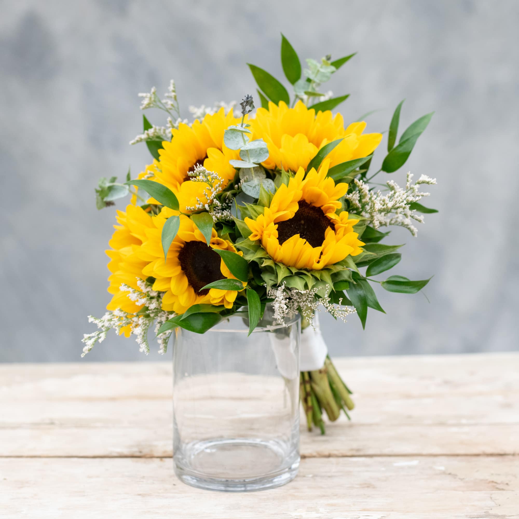 Bright and beautiful sunflowers mixed with delicate greenery and white accented flowers.