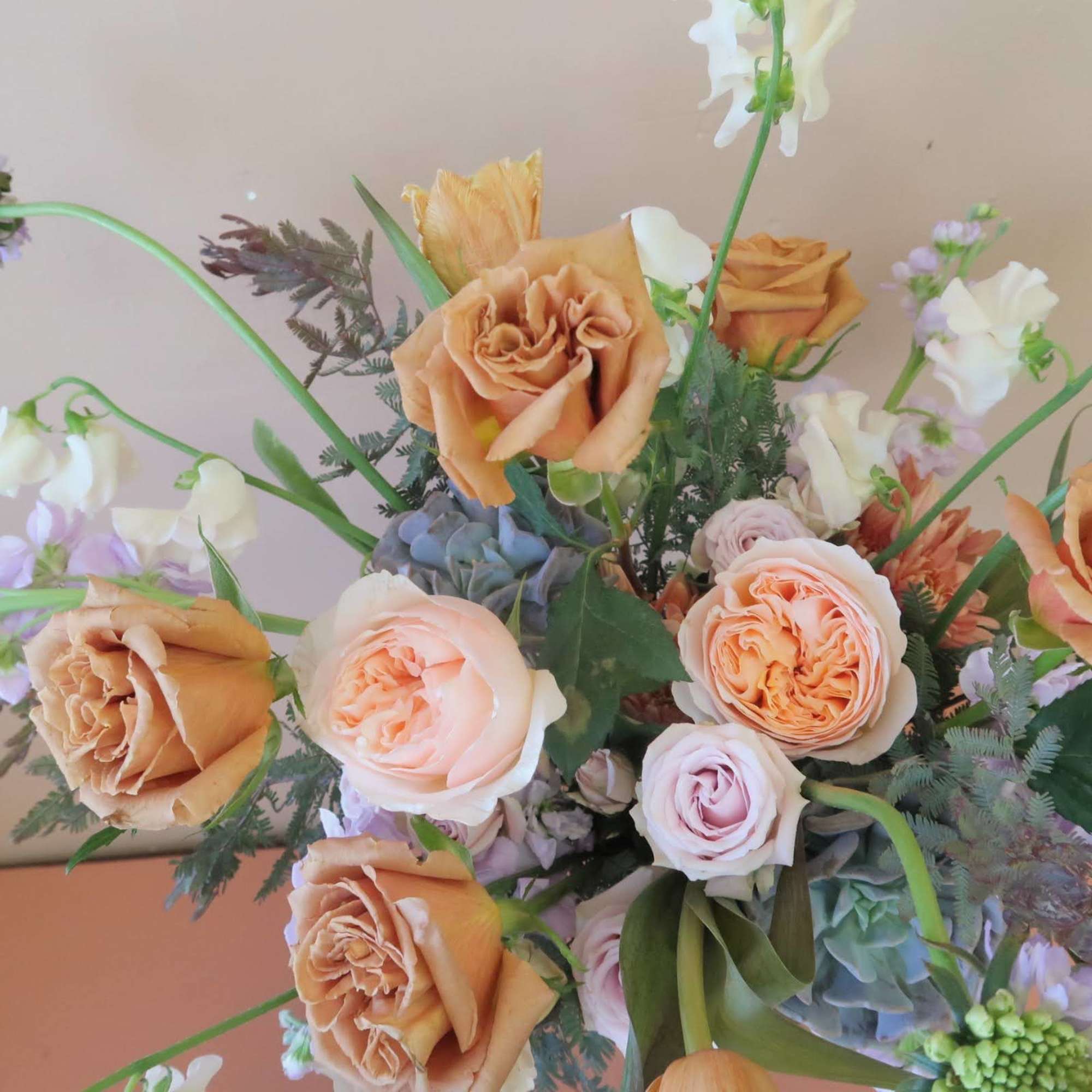 A soft hued arrangement featuring trendy toffee roses and lavender hues with