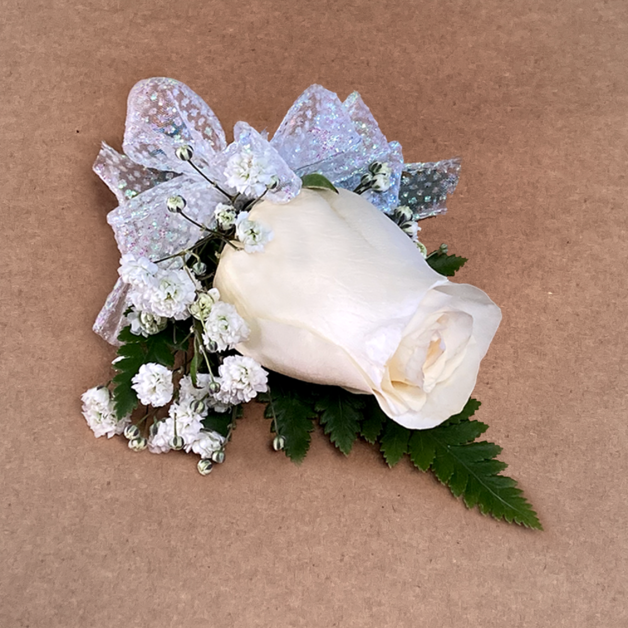 Our boutonni&egrave;re features a rose, baby&#039;s breath and freshly-cut greens. Accented with