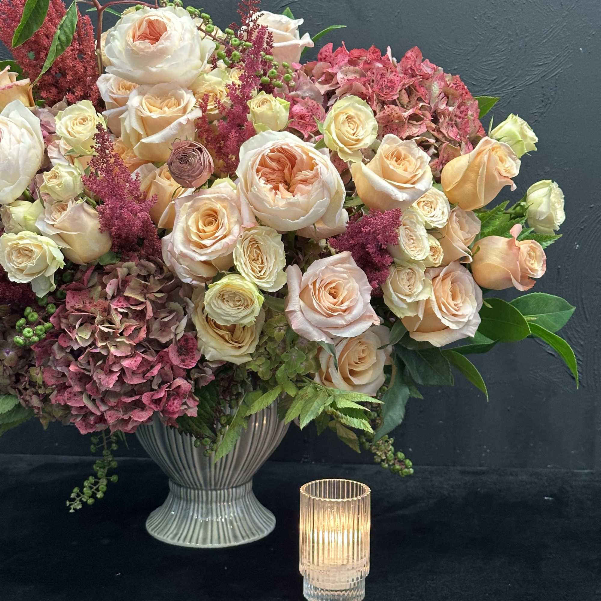 This stunning arrangement showcases peach garden roses, lush hydrangeas, and delicate spray