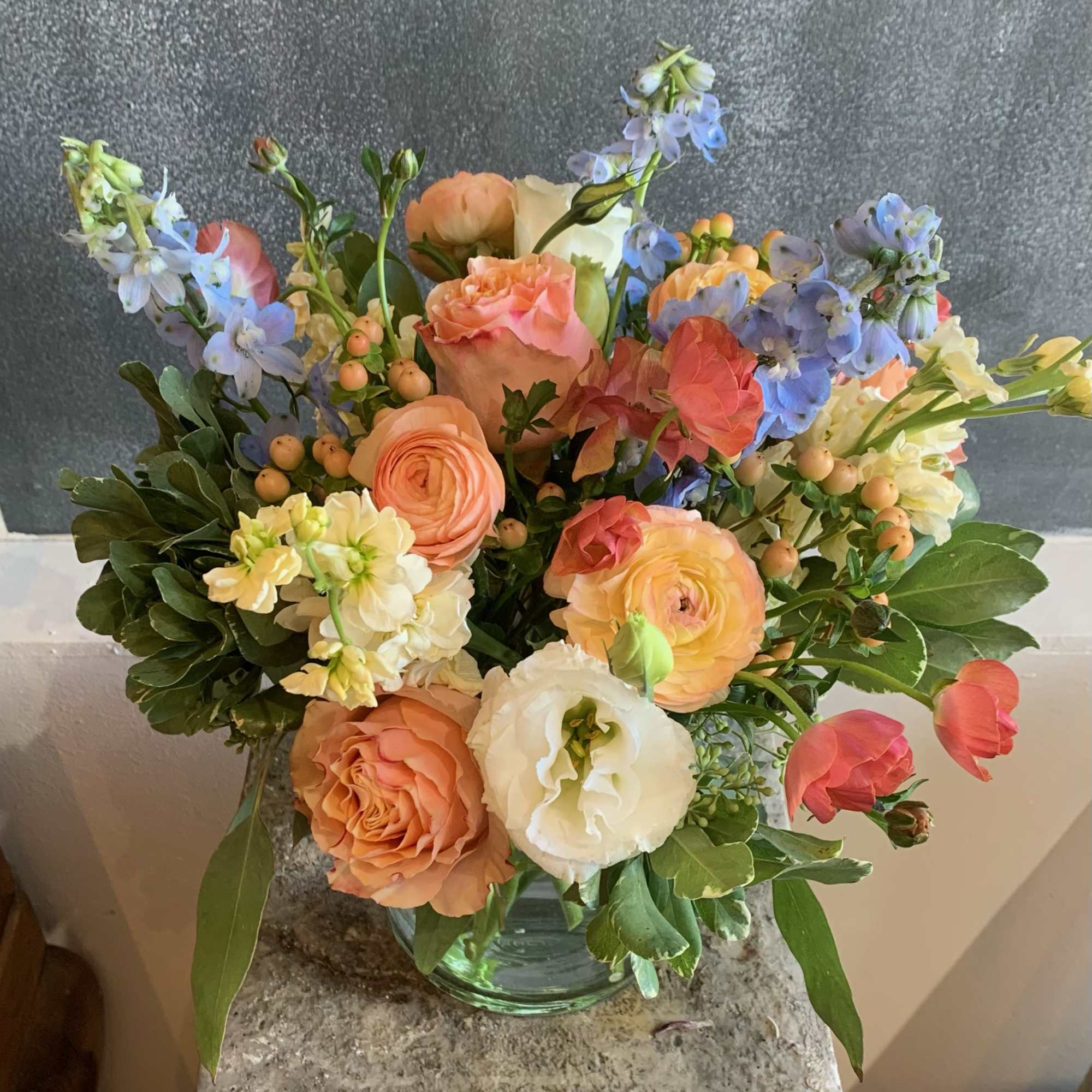 With pops of blue and orange, stunning imported Ranunculus and Roses make