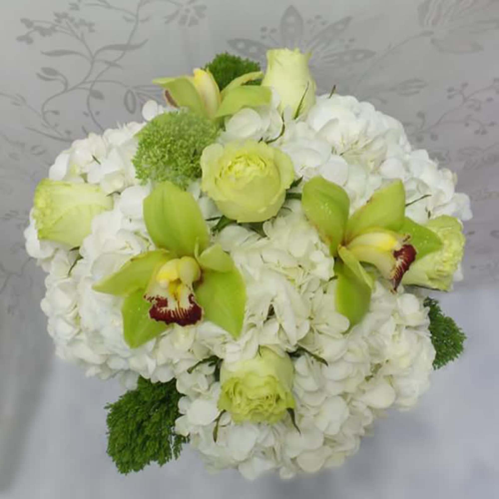 White hydrangeas, lime color roses, and cymbidium orchids arranged in a glass