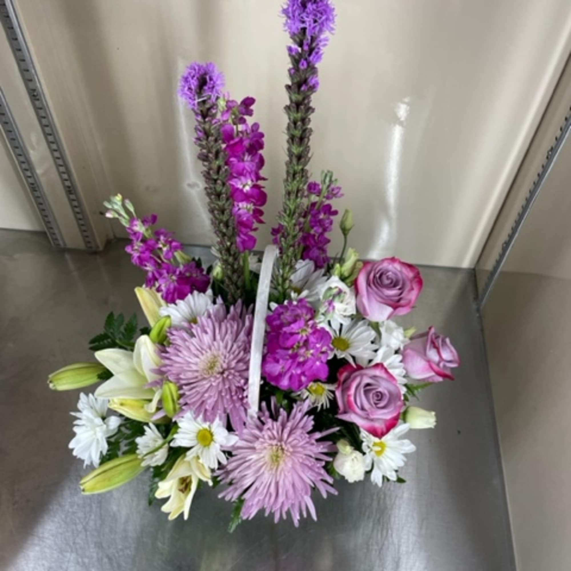 Mixed cut arrangement with purple and white flowers in a white basket.
