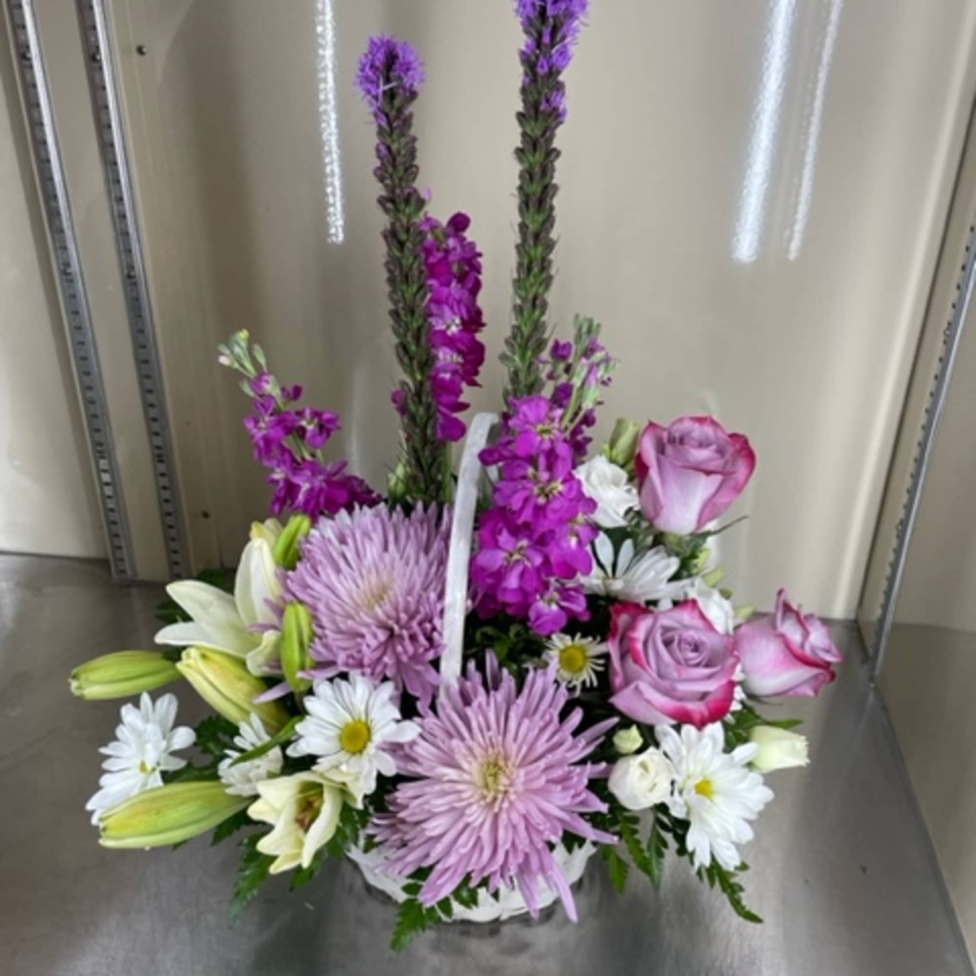 Mixed cut arrangement with purple and white flowers in a white basket.